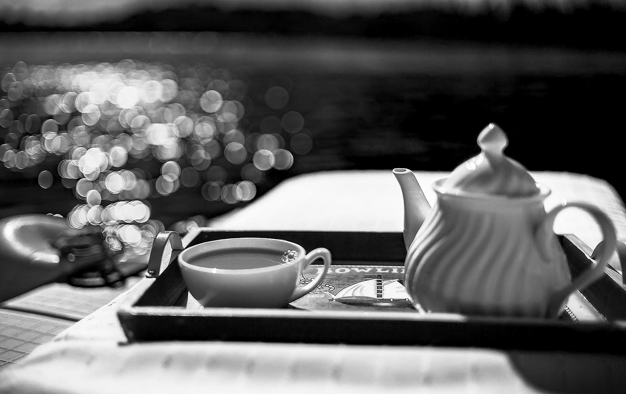 Black and white photo of a tea set on a tray, including a teapot and a cup, with a bokeh effect in the background.
