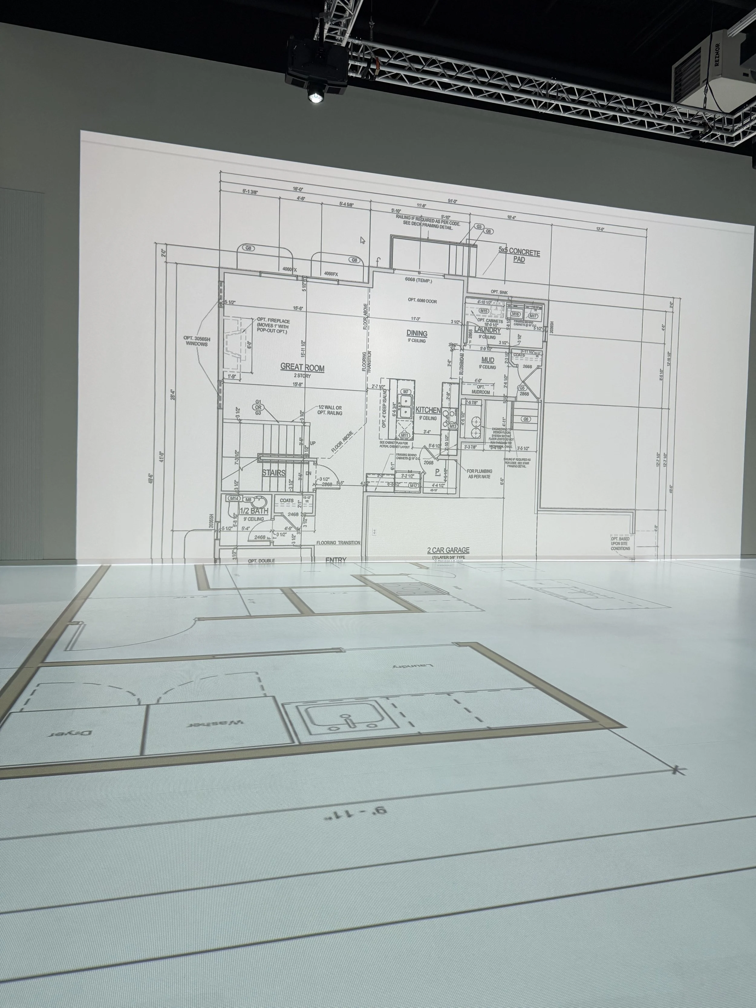Architectural blueprint projected on a wall showing floor plan details for a residential house, including rooms like great room, kitchen, dining, laundry, mudroom, and garage.
