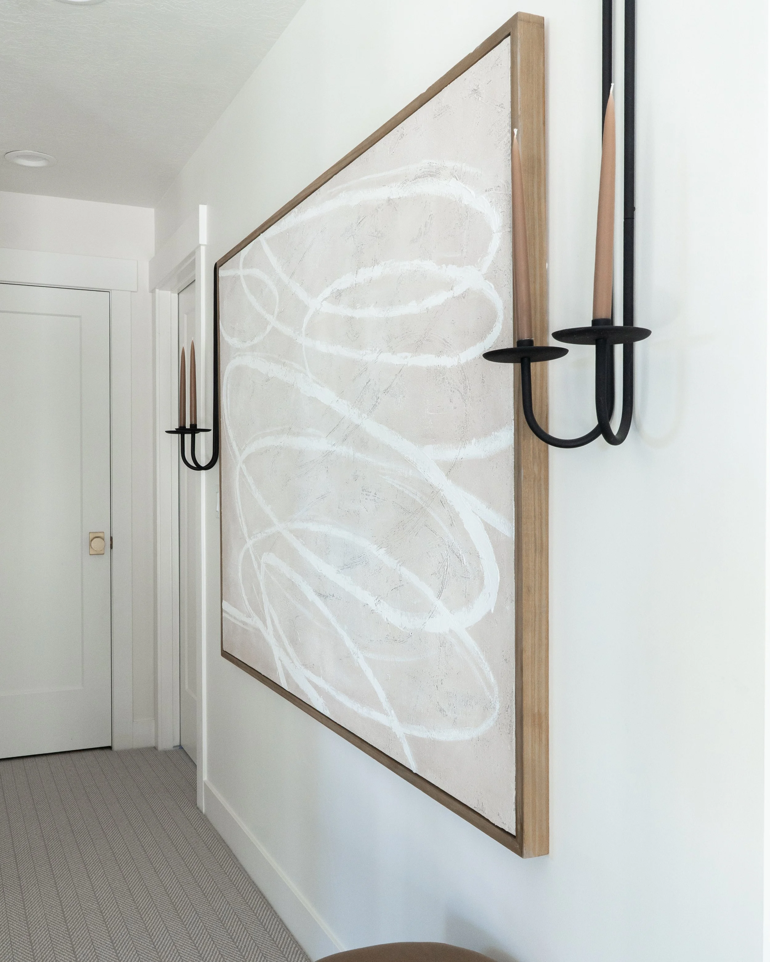 A blank canvas with white abstract swirl patterns leaning against a white wall, decorated with black wall-mounted candle holders with unlit candles.