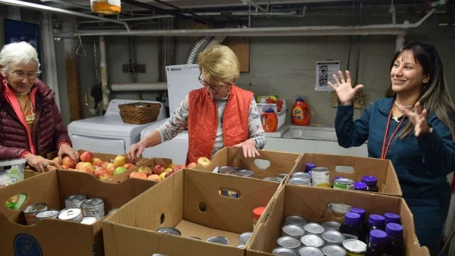 Three women sorting and organizing groceries in a storage or donation center.