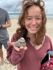 Smiling girl holding a small, gray, textured object on a beach