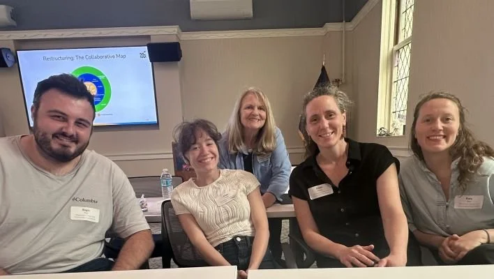 Five people smiling and posing for a photo in a conference room with a presentation slide on a screen behind them.