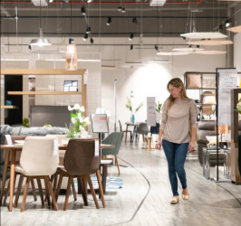 Woman in a store walking past a dining table and chairs..
