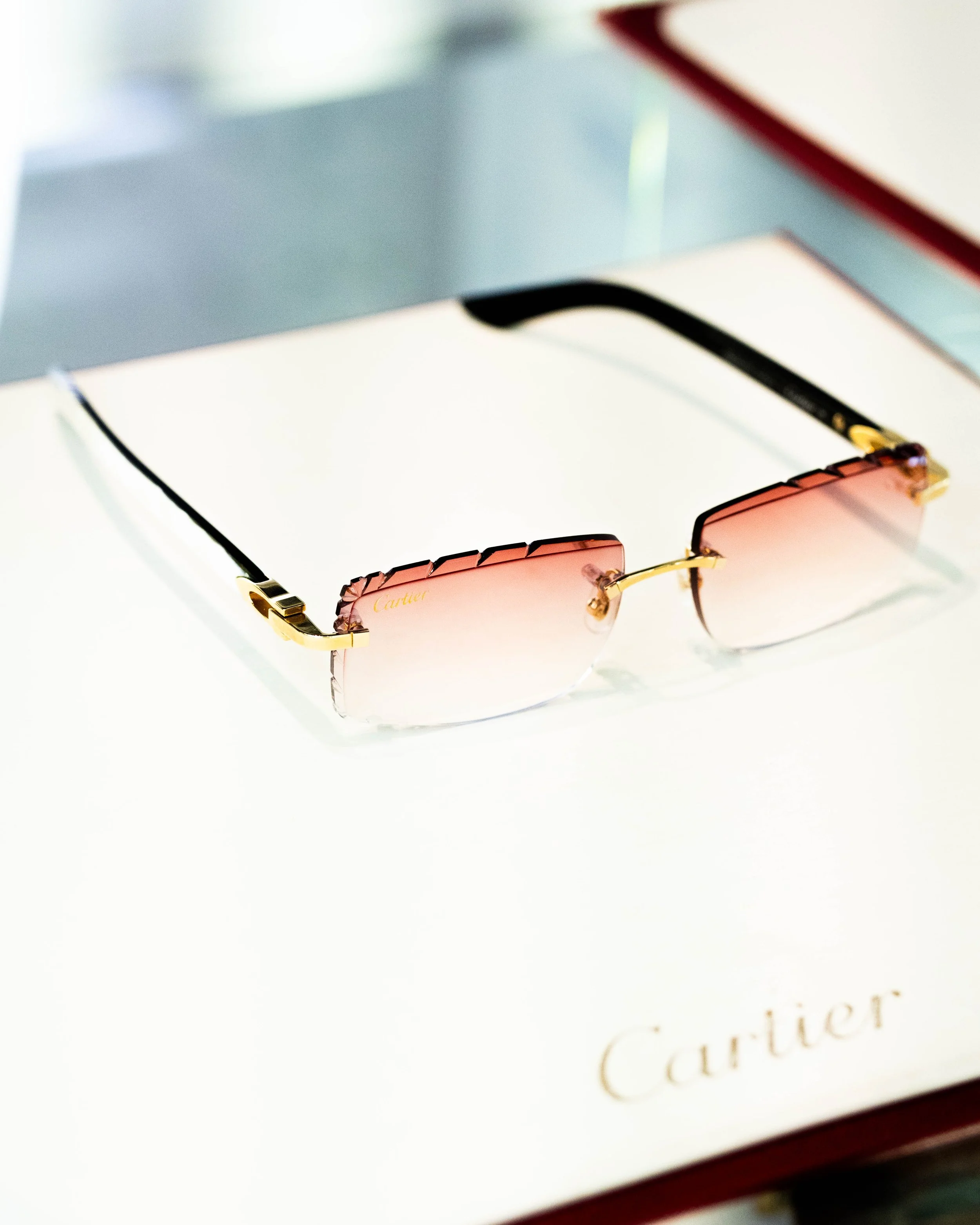 Close-up of pink Cartier sunglasses with gold accents on a white jewelry box, with a blurred background.