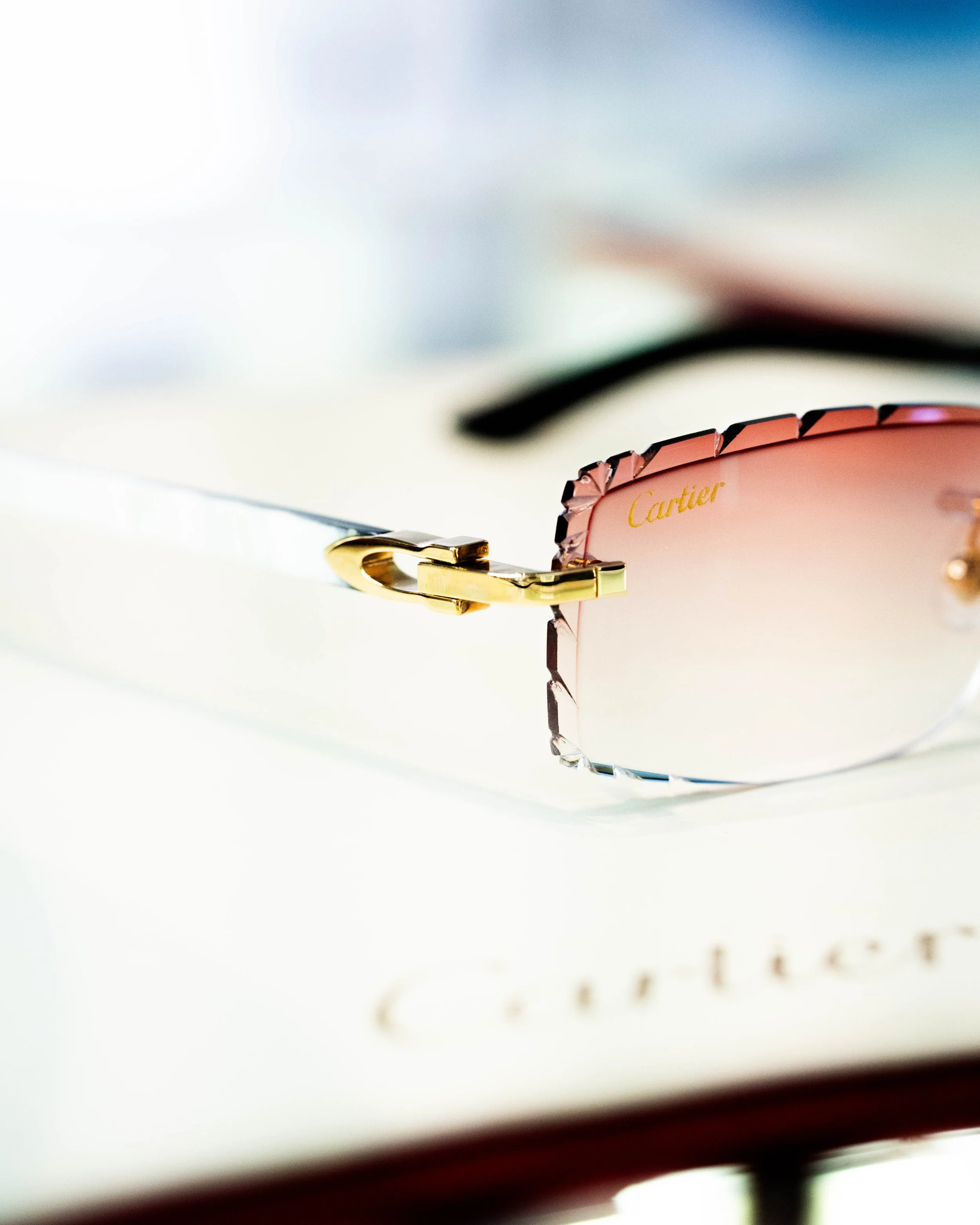 Close-up of a pink Cartier accessory, likely a sunglass or eyeglass frame, with gold accents, resting on a white surface with partially visible text.