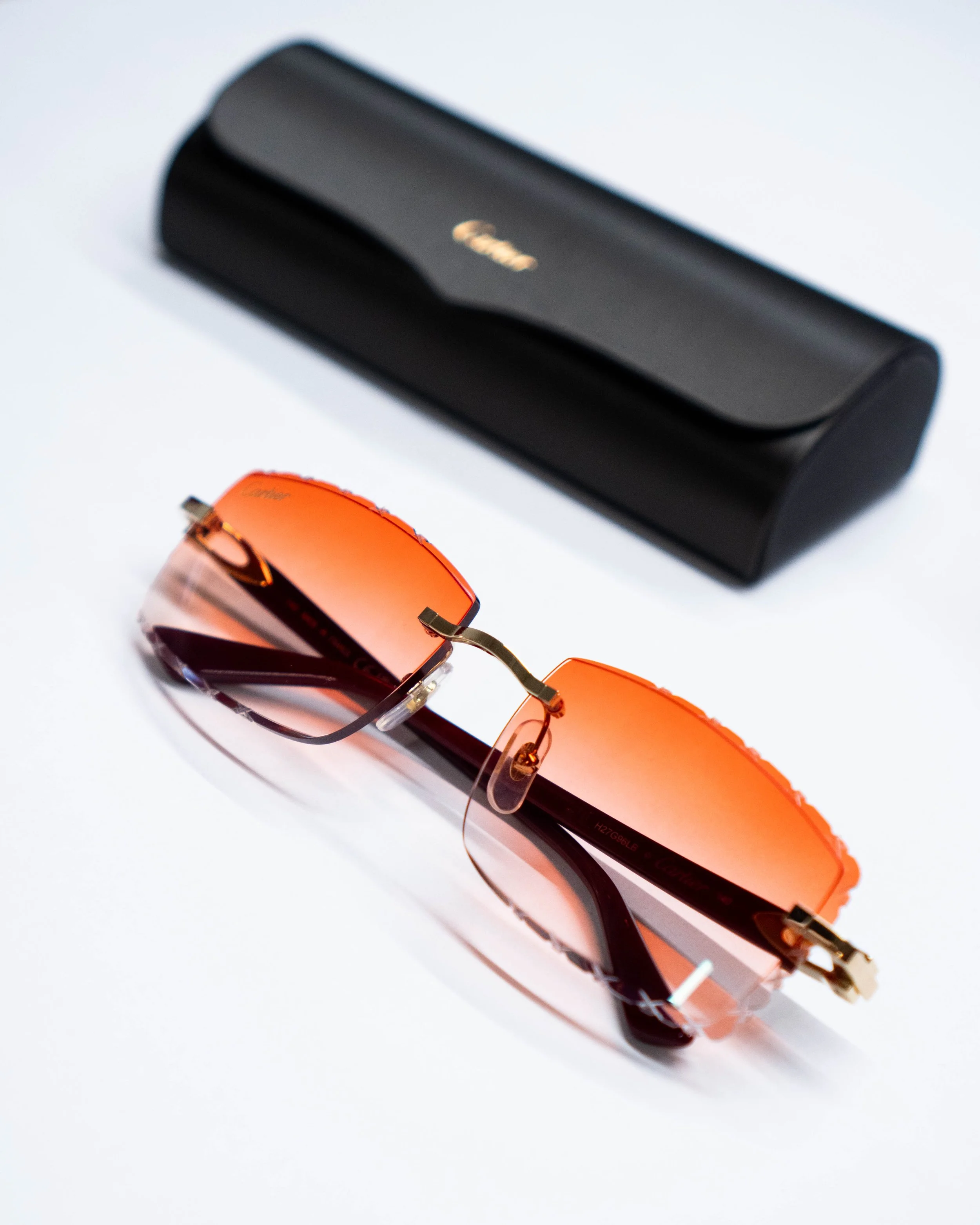 Black Canon eyeglass case and orange sunglasses with black lenses on white background.