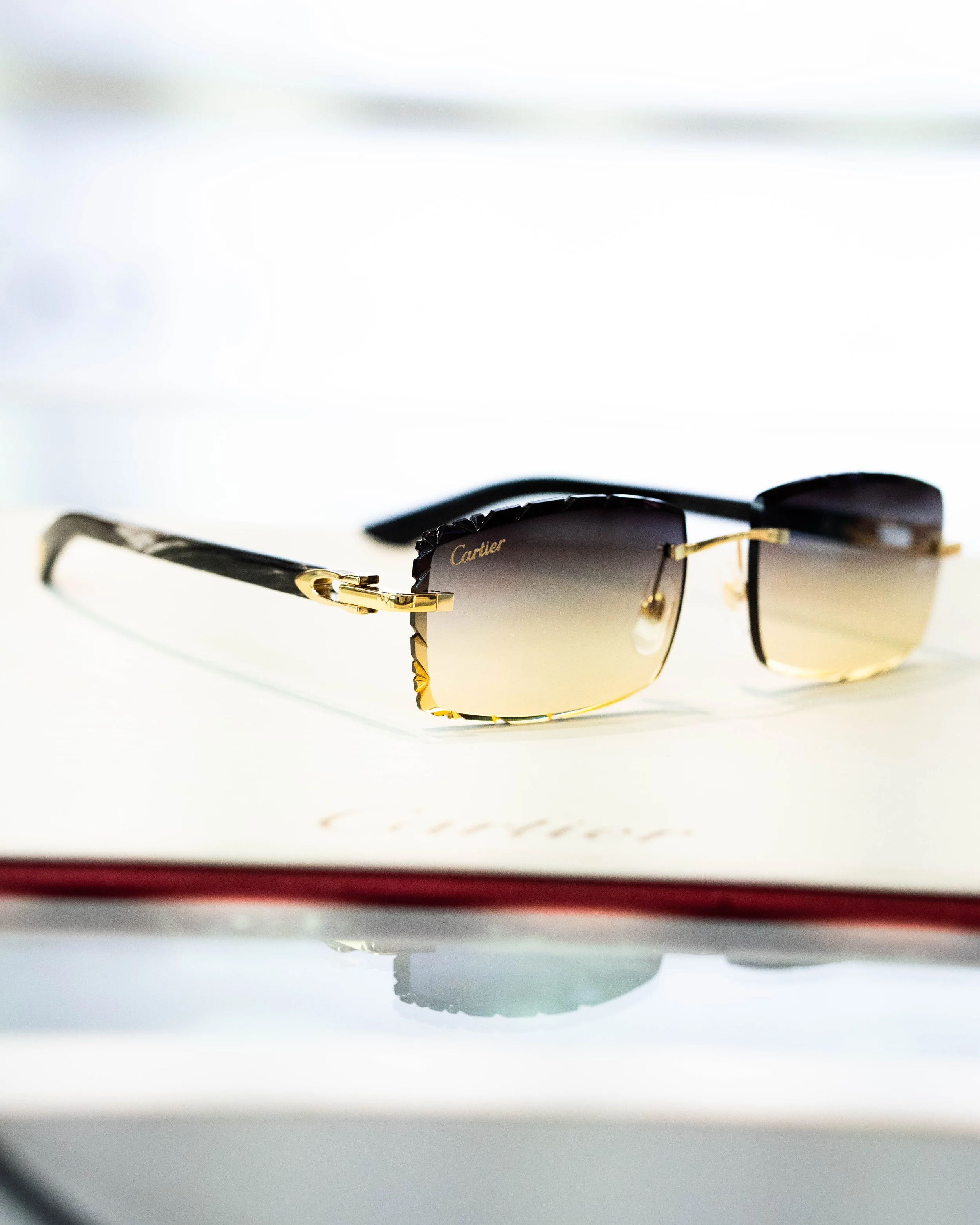 Close-up of a pair of sunglasses with gold accents on a white surface, reflecting the word Cartier.