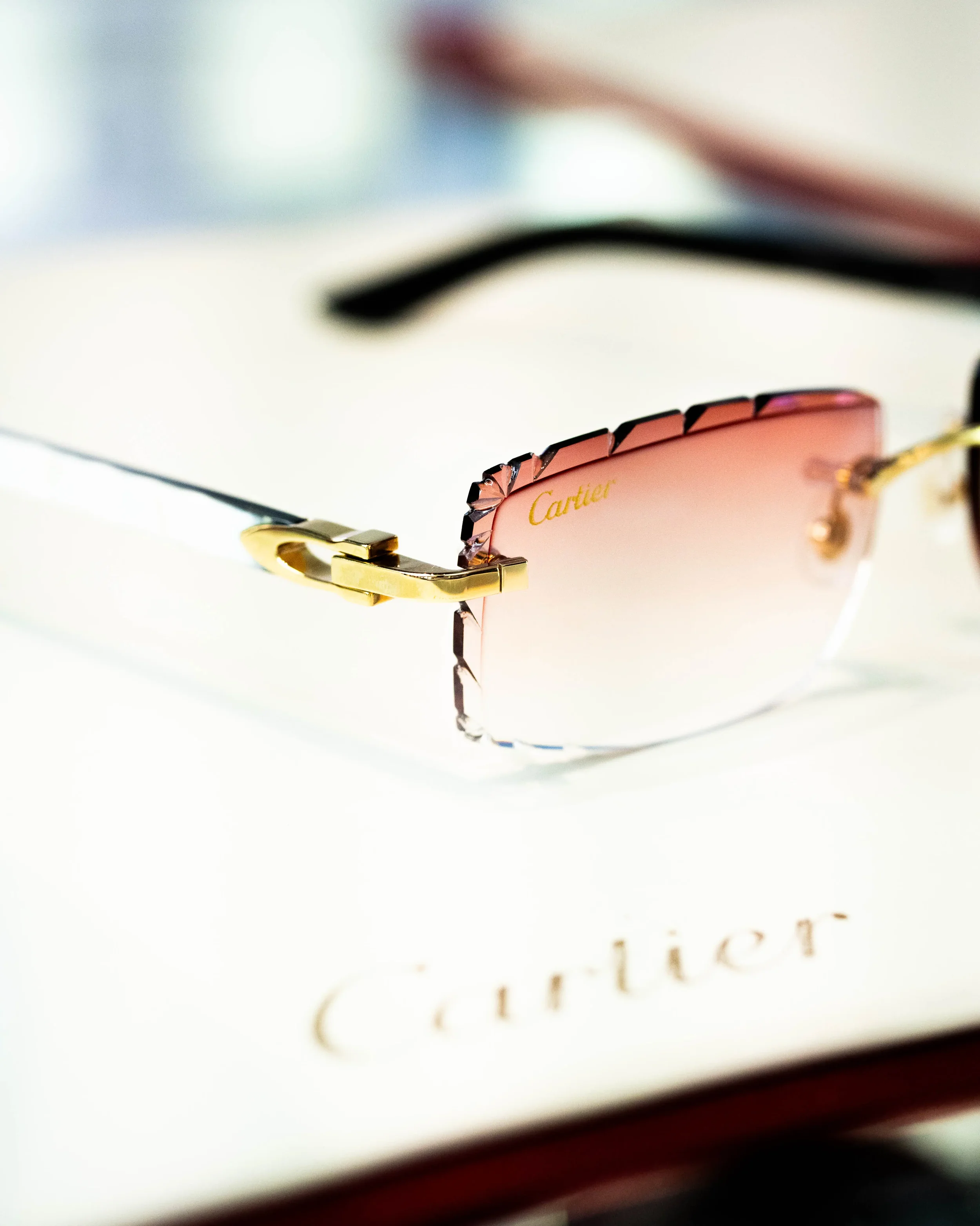 Close-up of a pair of sunglasses with pink lenses and gold hinges, with the brand name 'Cartier' visible on the frame, resting on a white surface.