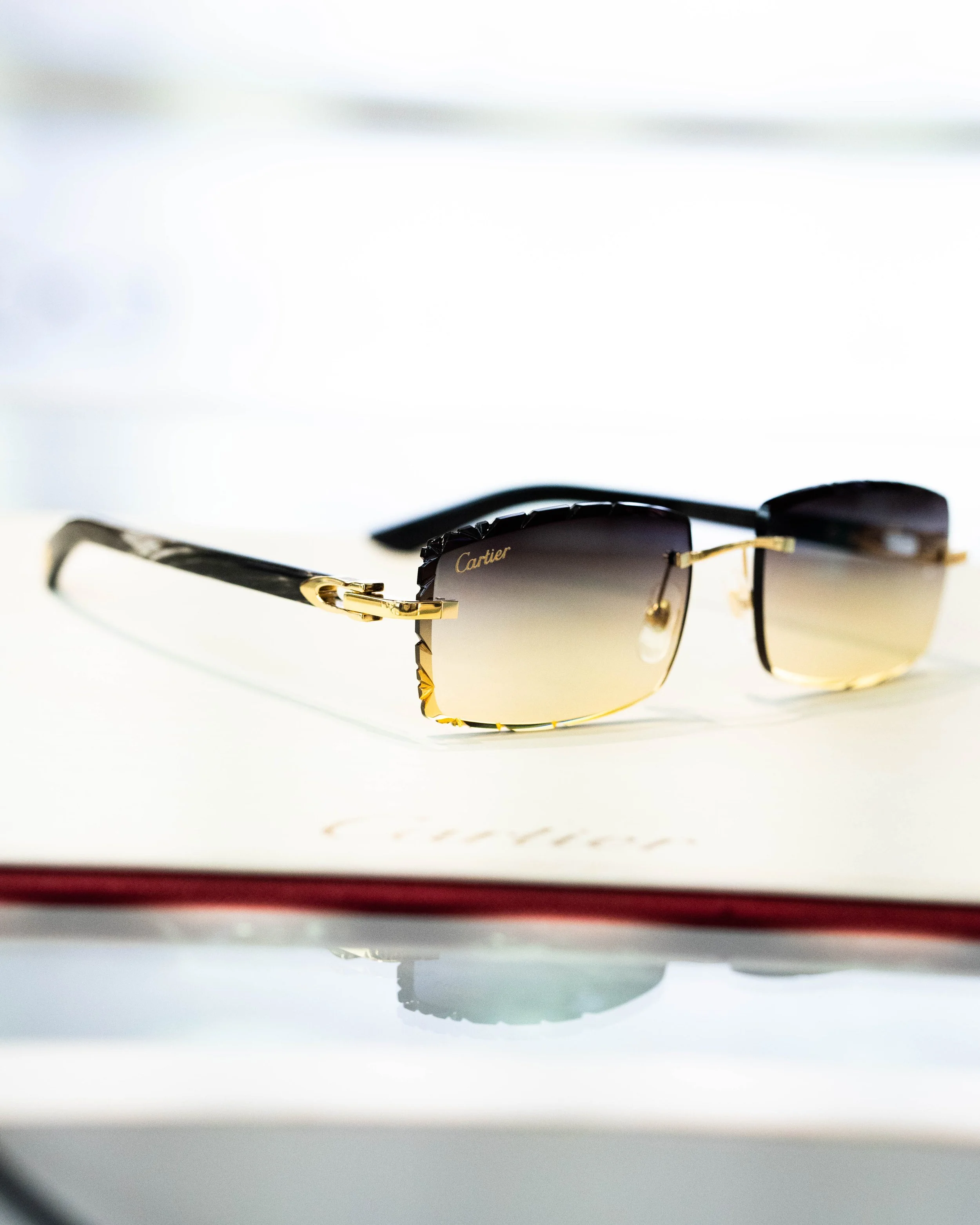 A pair of Cartier sunglasses with black frames and gold accents on a white surface. The reflection of light is visible on the lenses.