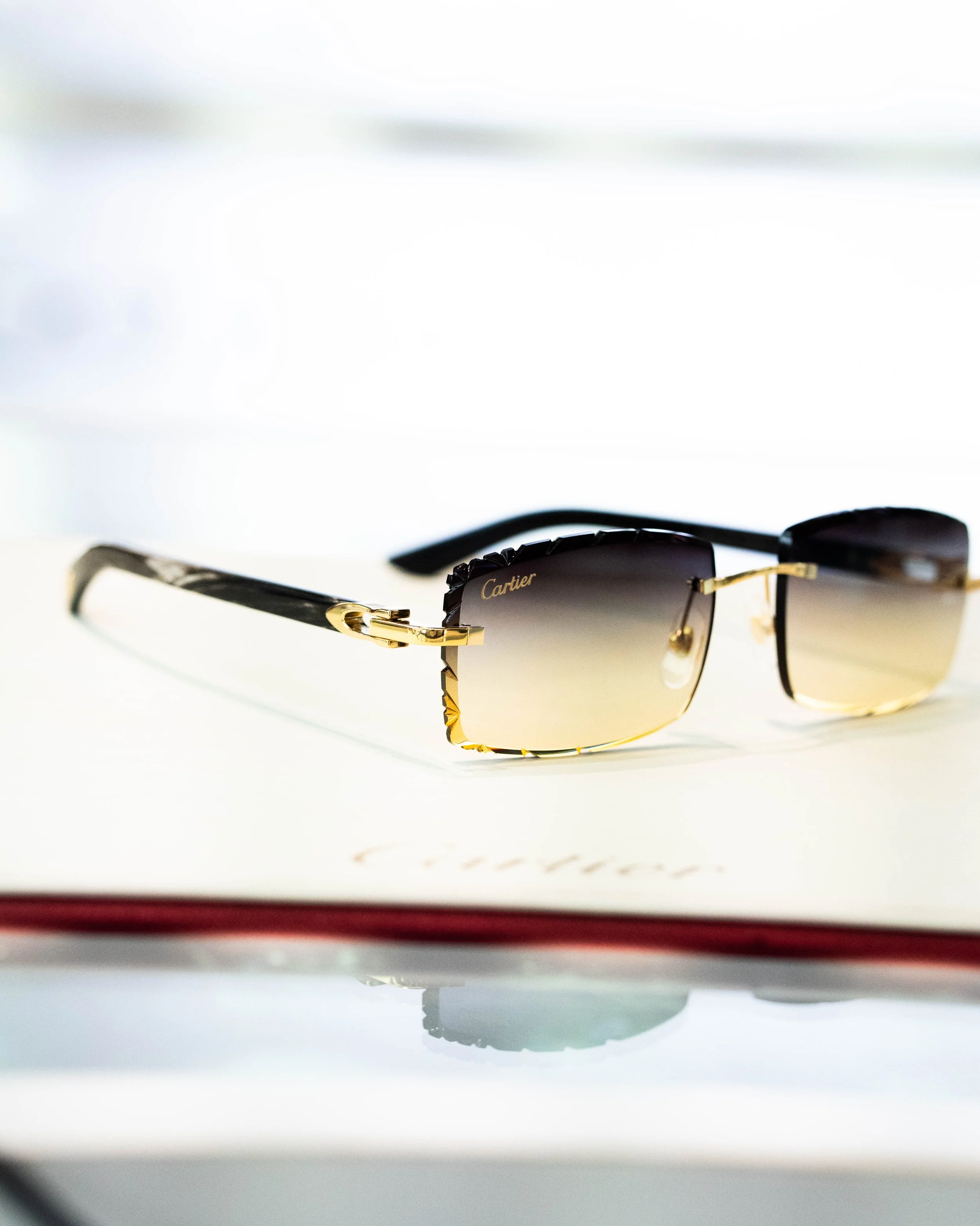 A pair of Cartier sunglasses with black and gold accents resting on a white surface, with a faint shadow underneath.