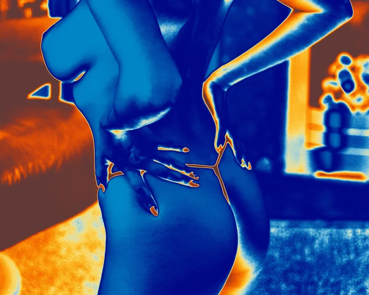 Color-enhanced photo of a woman with her hand on her hip, posing in front of a blurred background with shelves and decorative items. Nude Art Photography by Vlad Goth.