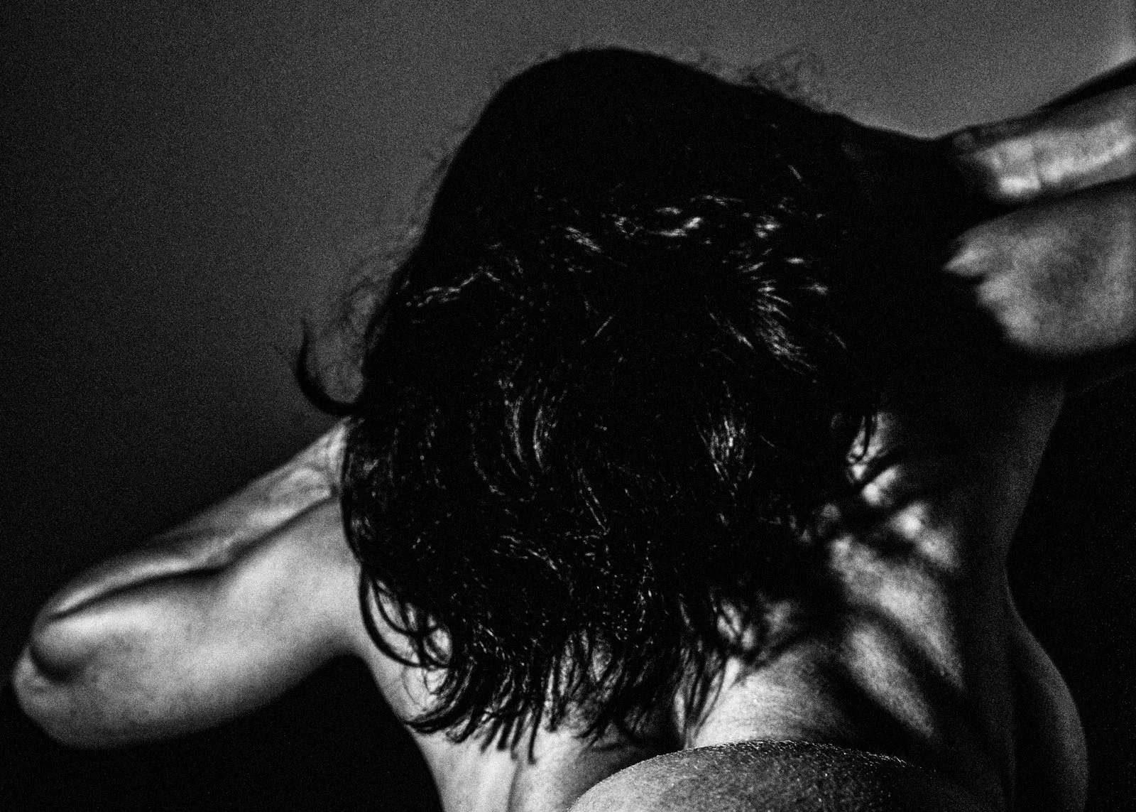Black and white photo of a woman with deep dark hair covering her back, with one arm raised and resting on their head. Nude Art Photography by Vlad Goth.