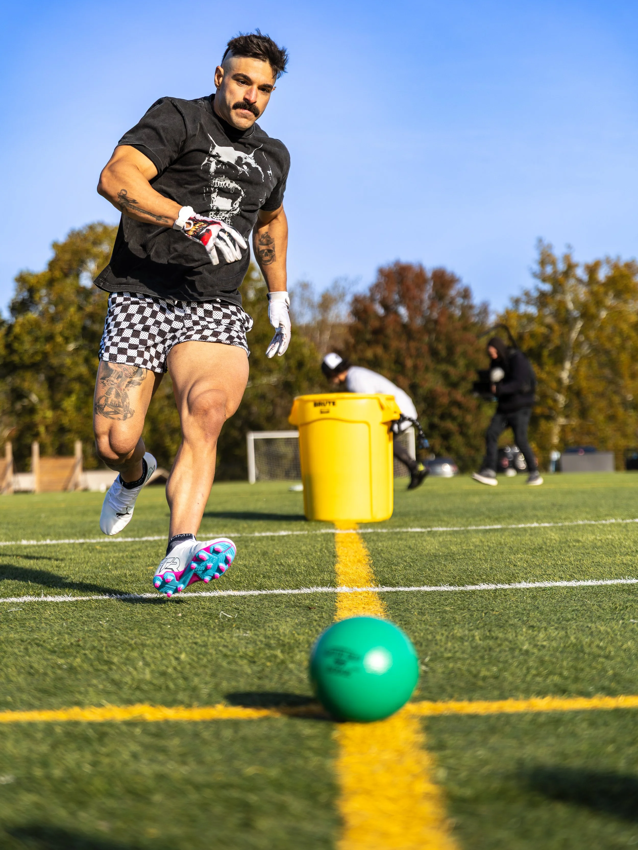 A man in athletic shorts and a T-shirt playing field hockey on a grass field.
