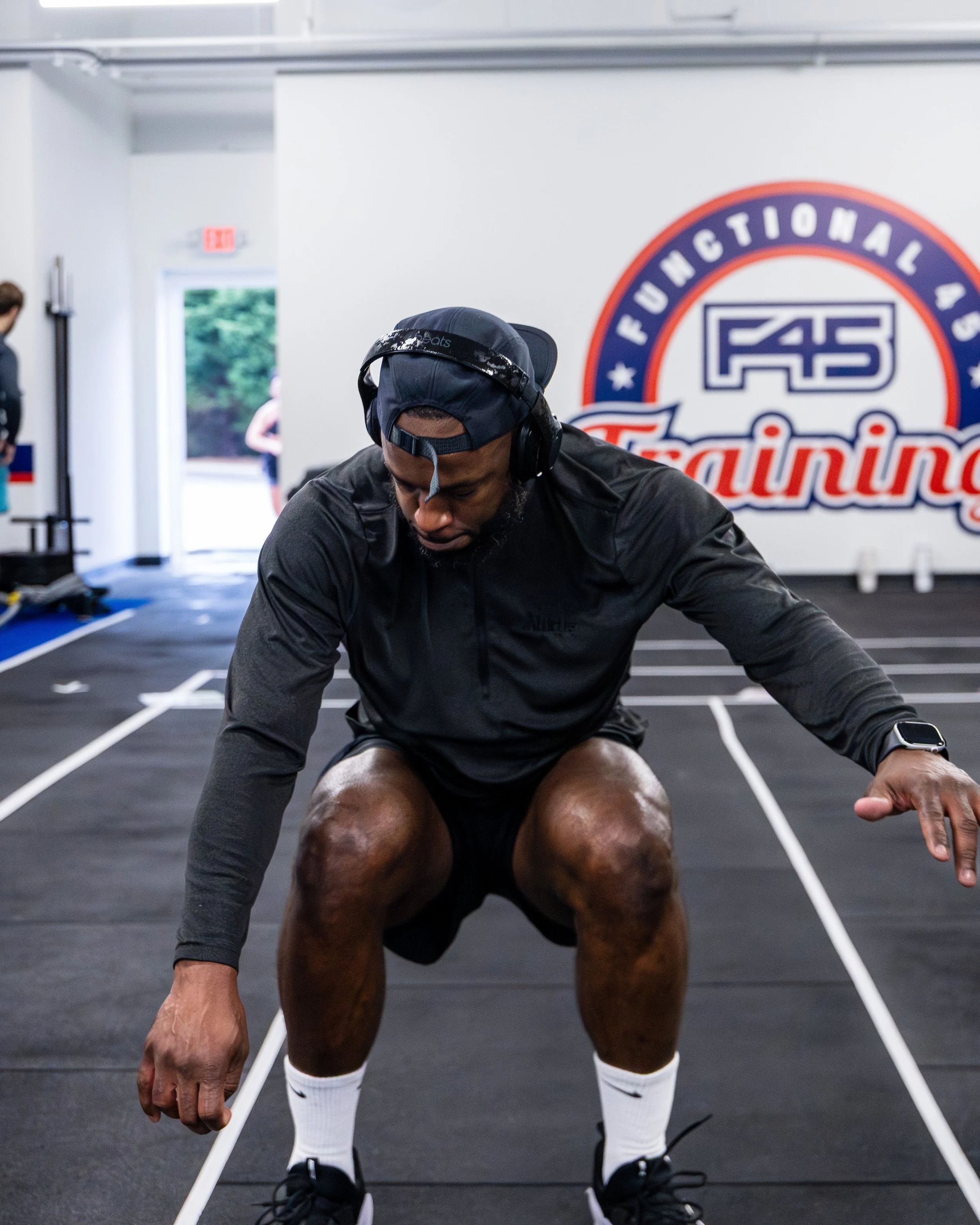 A person wearing a black cap, headphones, a black long-sleeve shirt, and white socks shown in a gym with a logo on the wall that reads "FUTURISTIC ATHLETICS".