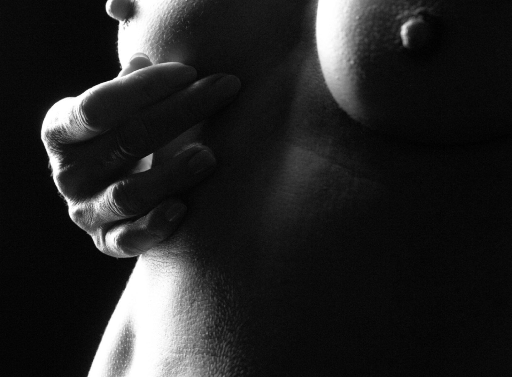 Close-up black and white image of a person’s chest with a hand touching the clavicle area, focusing on natural skin texture and shadows.