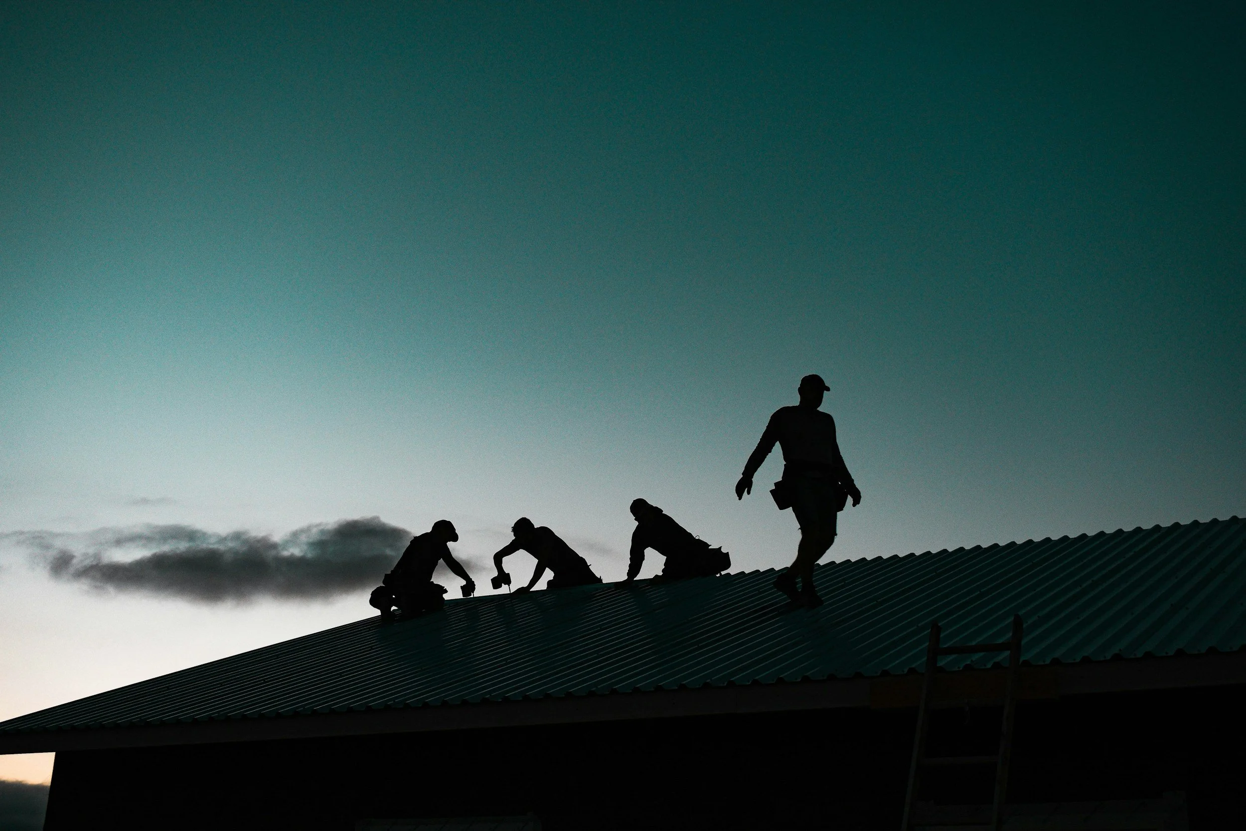 A roofing company crew installing metal roof in dusk.