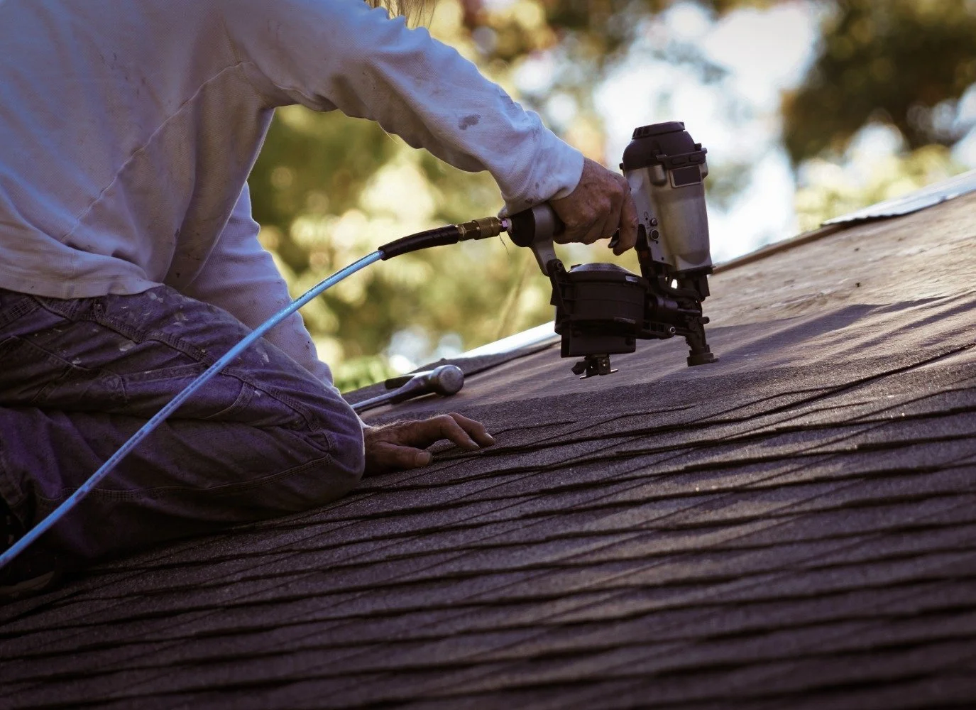Man with a power tool fixing a asphalt shingle roof in Bend Oregon
