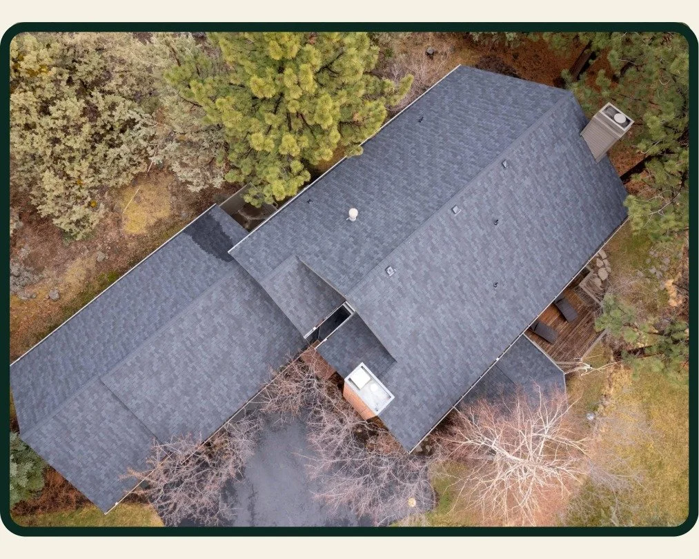 Asphalt shingle roof replacement in aerial photo by Bend Oregon roofing company McMurray & Sons of a home surrounded by trees