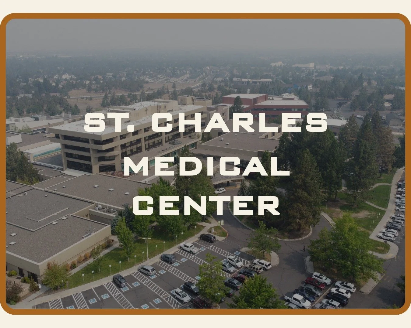 Aerial photo of St. Charles Medical Center with newly renewed roofs and parking lot surrounded by trees.