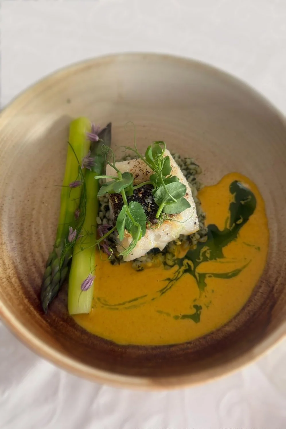 Gerechten met vis, een groene asperge, een saus en microgroenten op een kom in sertelt