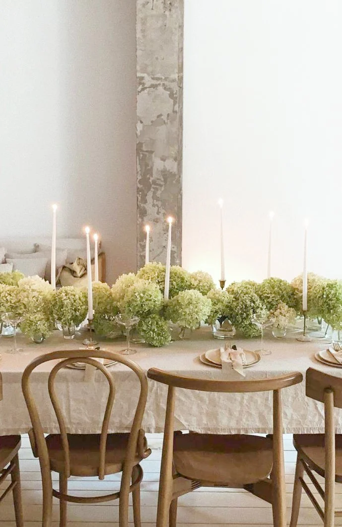 Een gedekte eettafel met witte bloemen en kaarsen, in een minimalistische inrichting.