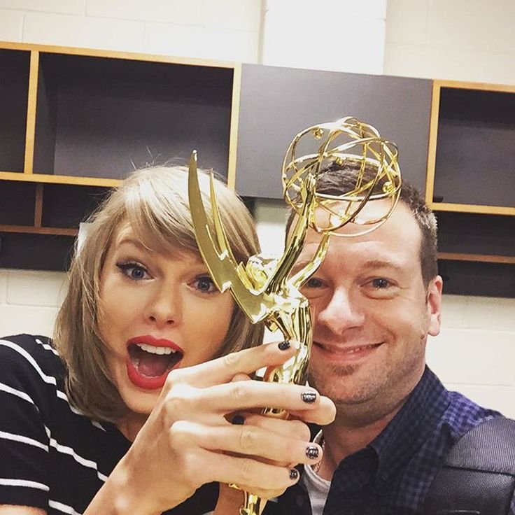 Taylor Swift and David Cook smiling and holding a Grammy award together in front of a bookshelf.