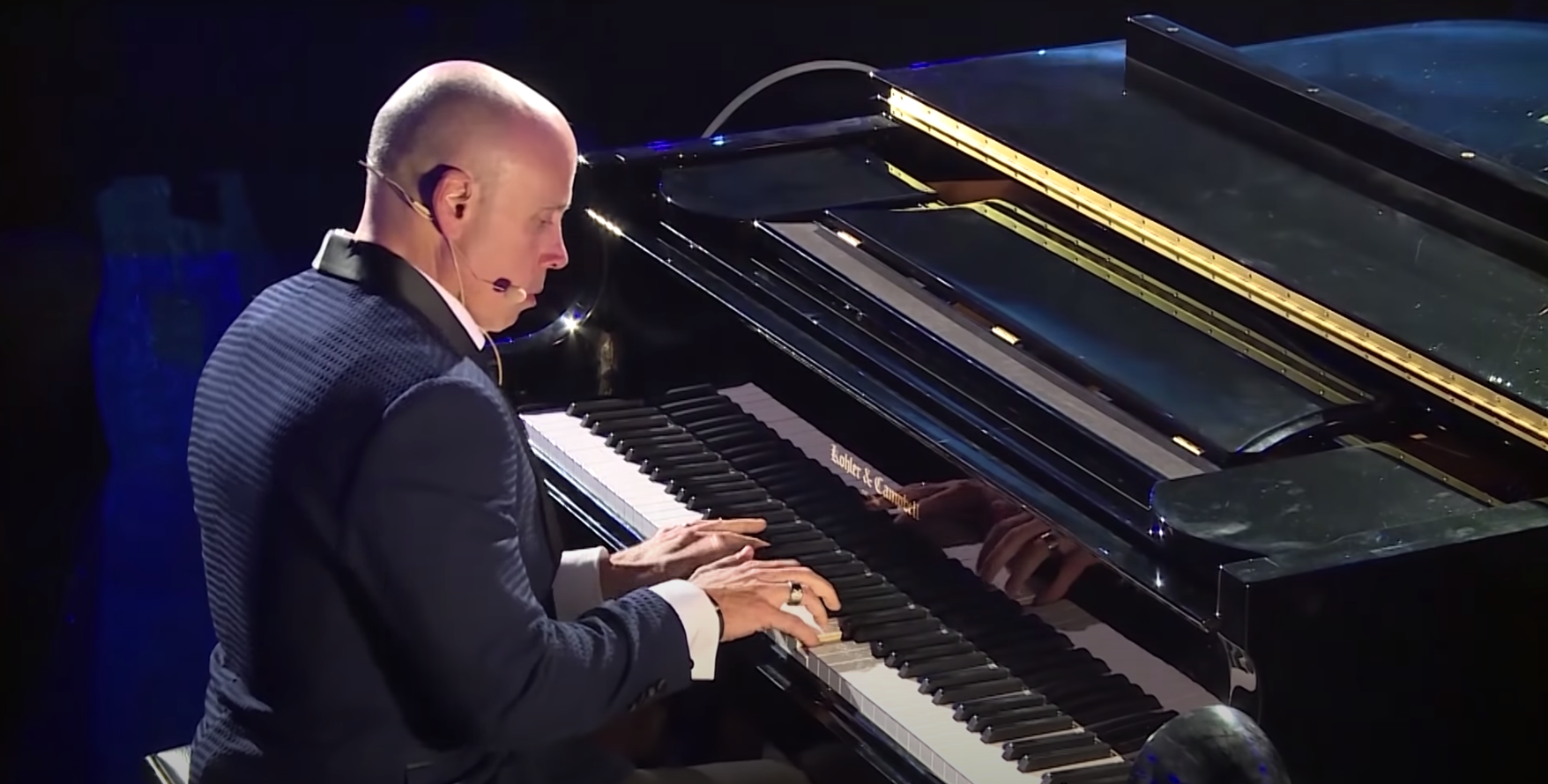 Kitt Wakeley in formal attire playing a grand piano on a stage.