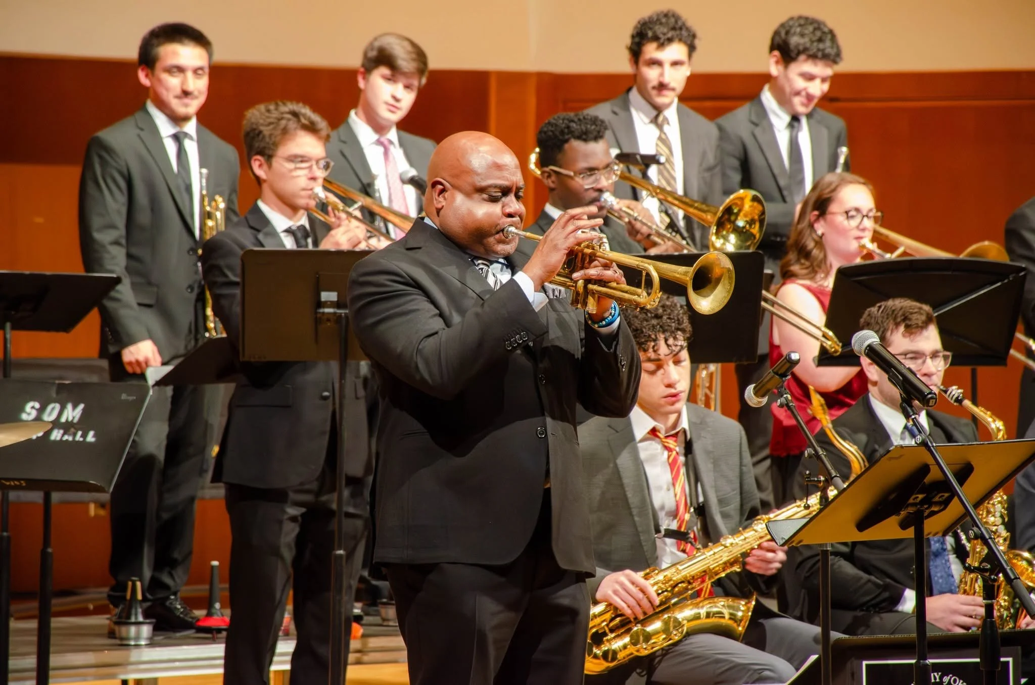 A group of musicians performing on stage, with Terell Stafford some playing saxophones and others playing trumpets, dressed in formal suits.