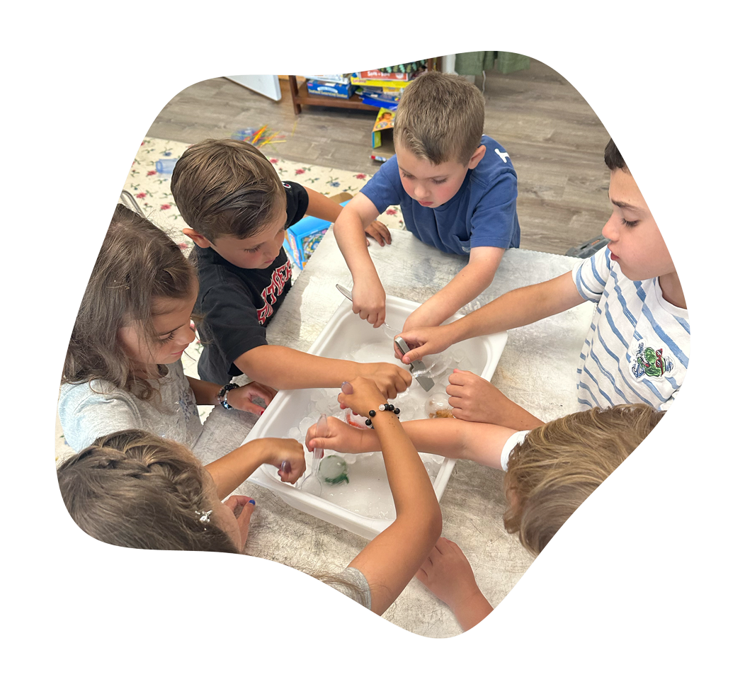 Children gathered around a table, playing with floating ice and toys in a water tray.