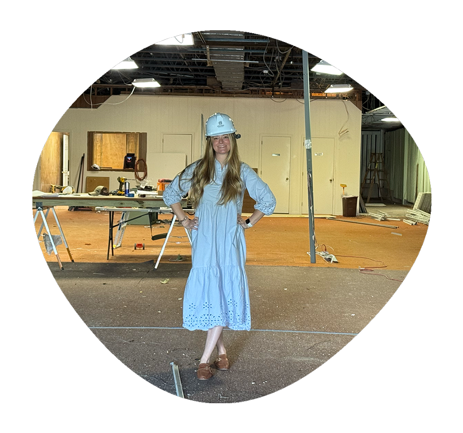 Lauren Miska in a blue dress and safety helmet standing with hands on hips inside a construction site.