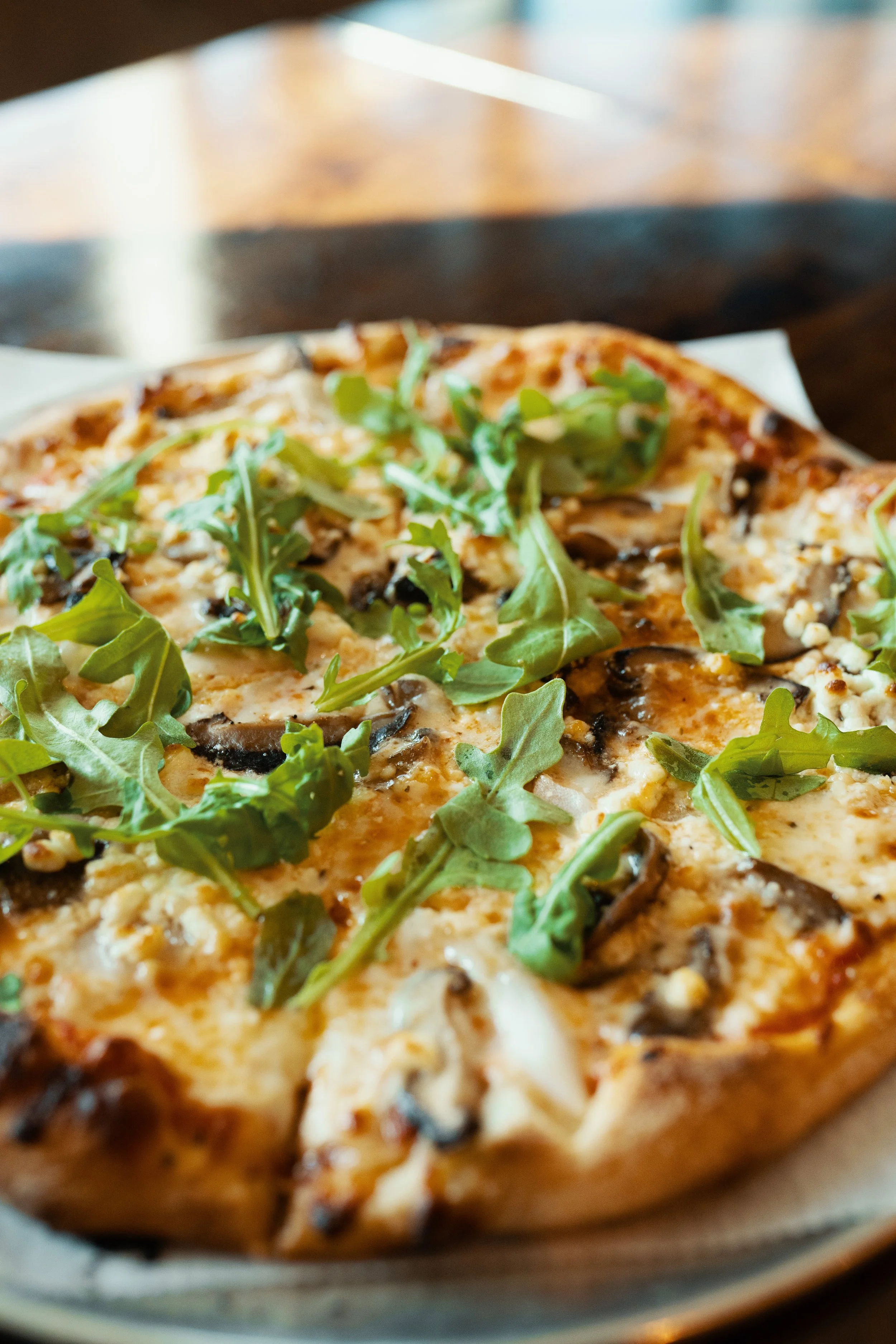 Close-up of a pizza topped with arugula, mushrooms, cheese, and other ingredients.