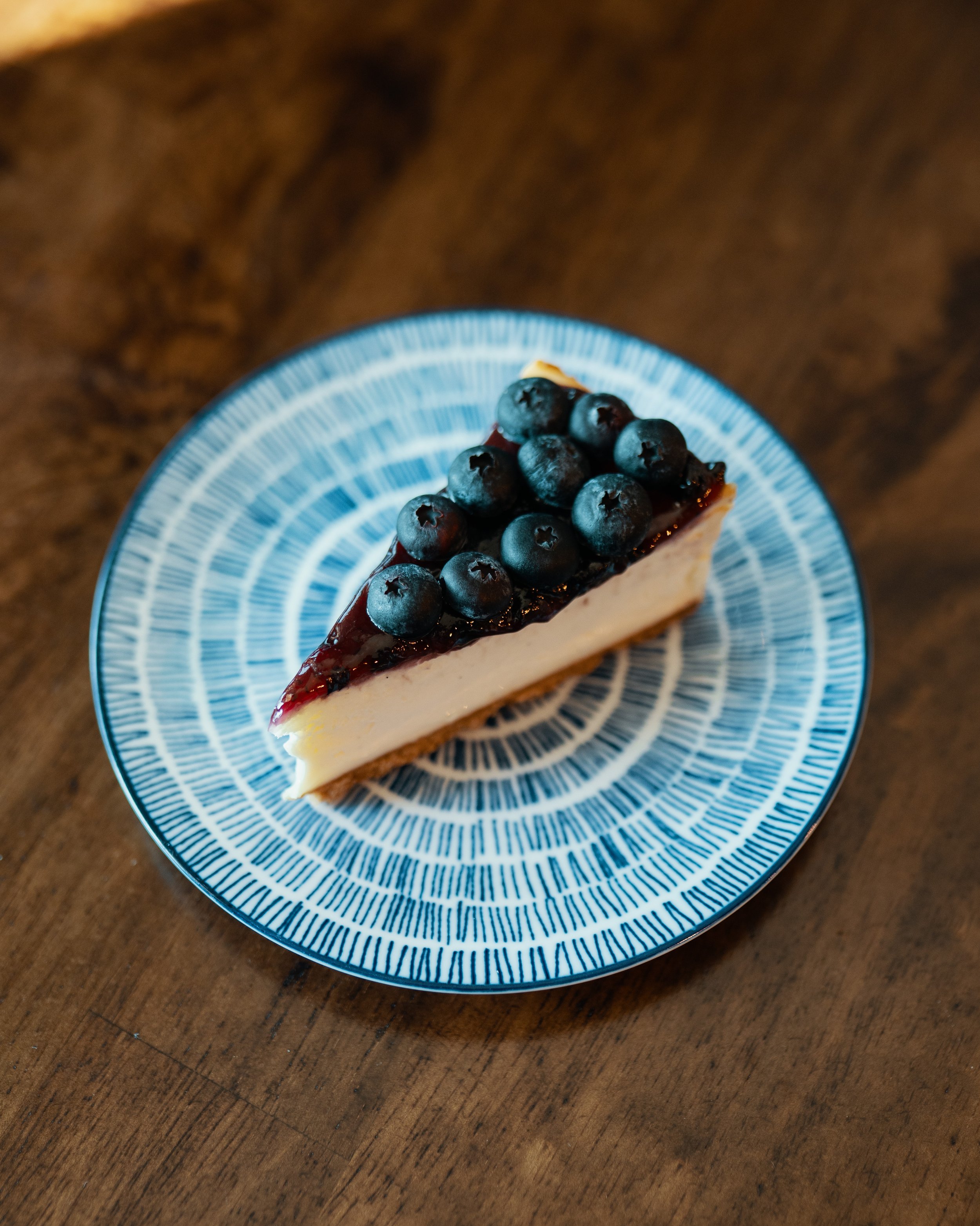 A slice of cheesecake topped with blueberries on a blue and white patterned plate.