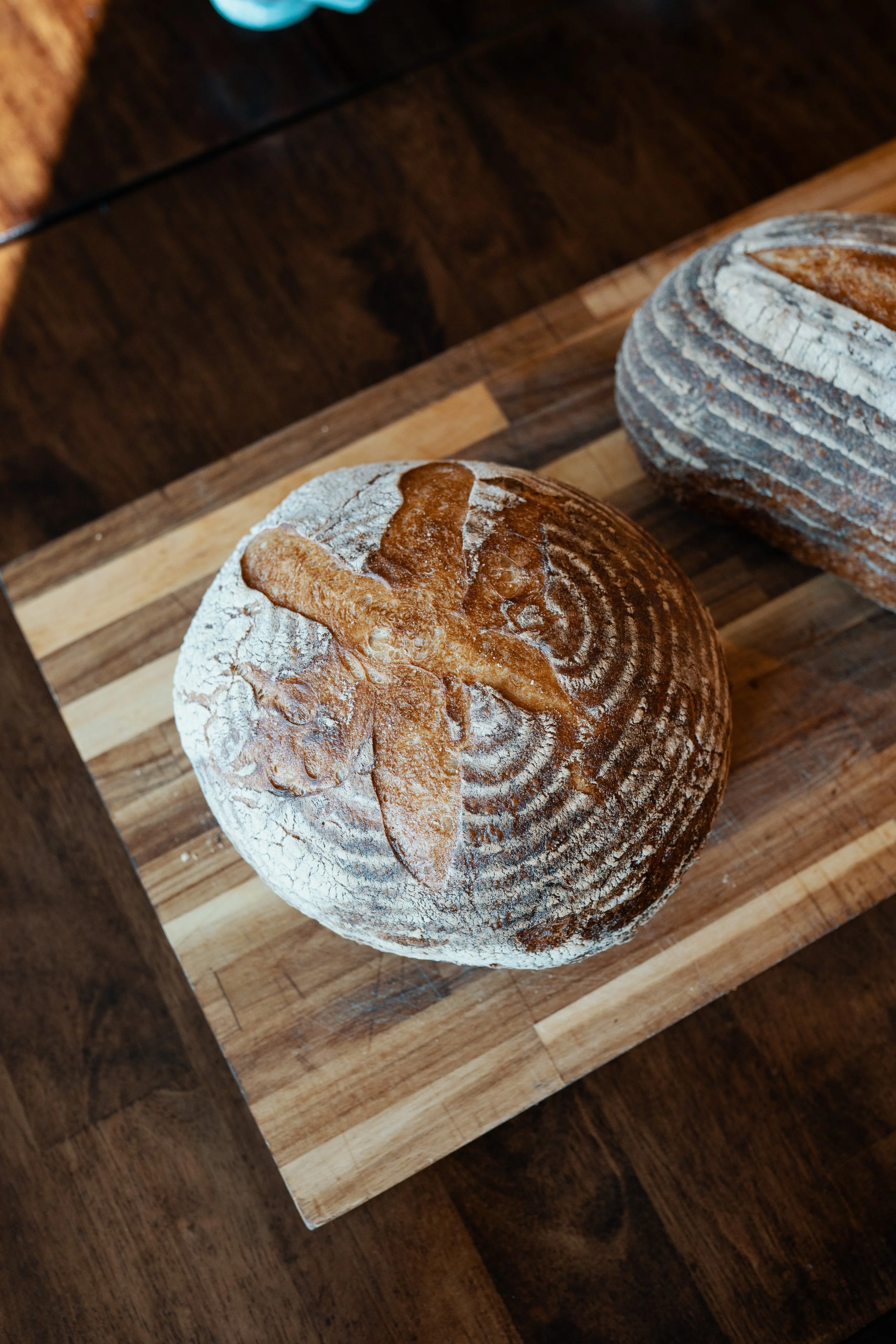 Two round loaves of rustic bread with flour dusting, placed on a wooden cutting board.
