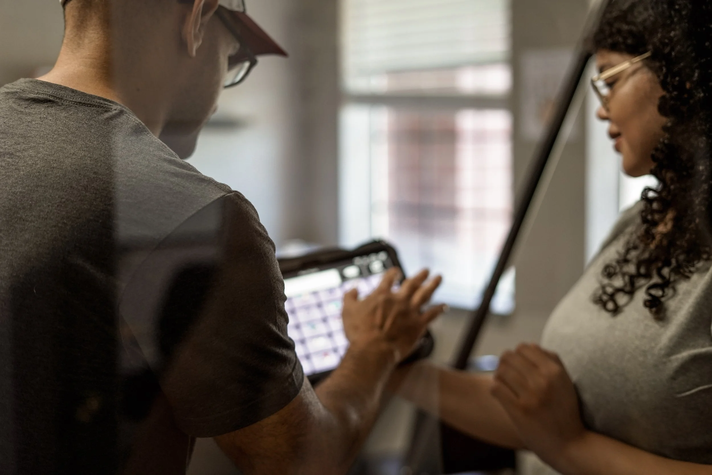 Two women are standing close together, looking at a tablet screen, with a window in the background.
