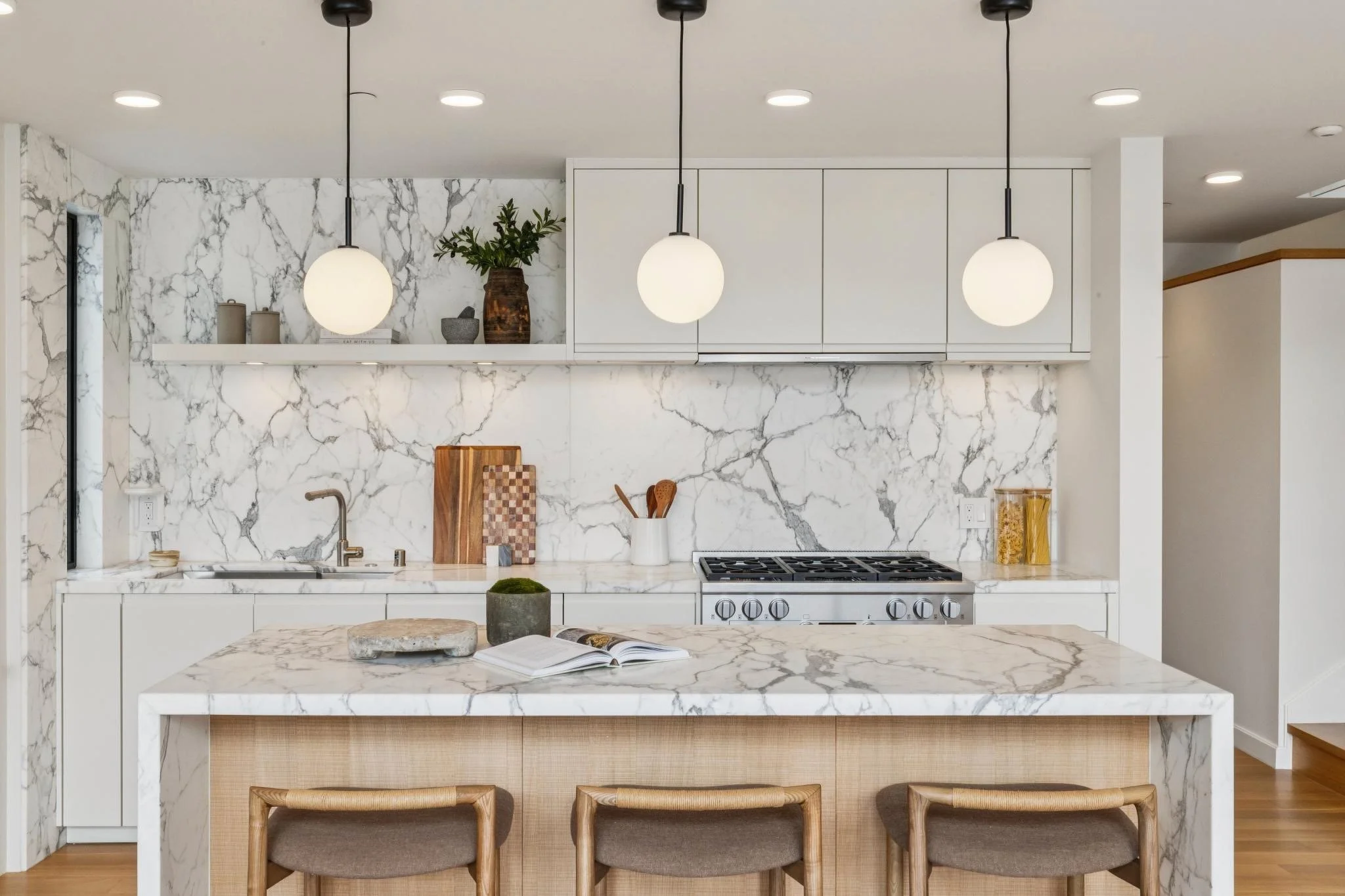 Modern kitchen with white marble countertops and backsplash, pendant lights, and wooden bar stools.