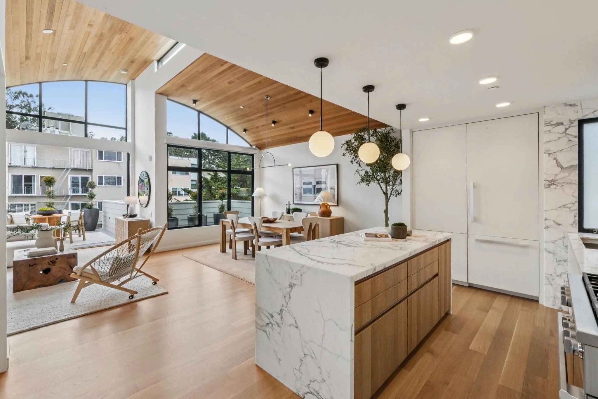 Modern open-concept kitchen and dining area with large windows, wooden accents, and marble countertops.