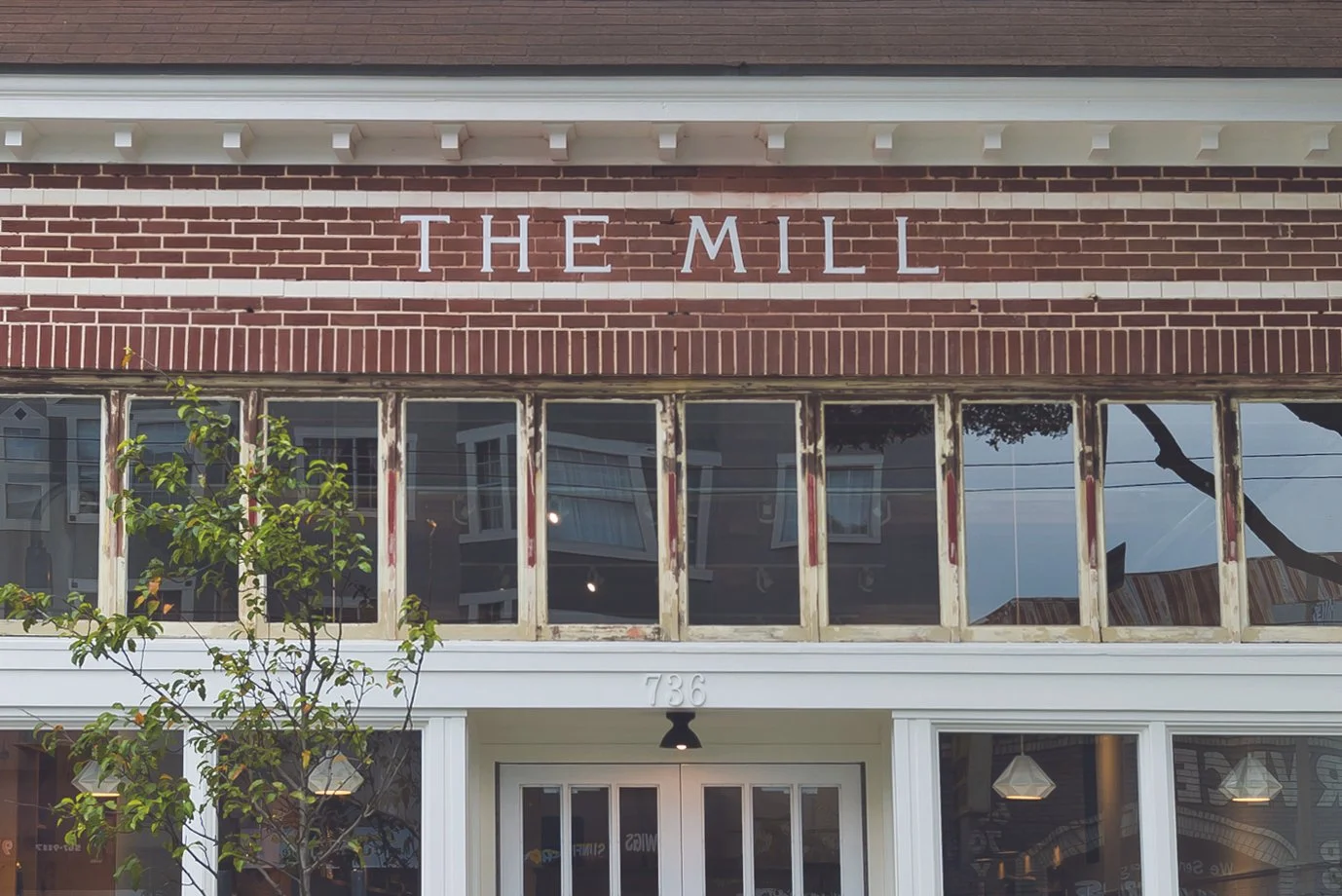 Exterior view of a brick building with signage that reads "THE MILL" above large front windows, and the street number 736 above the entrance.