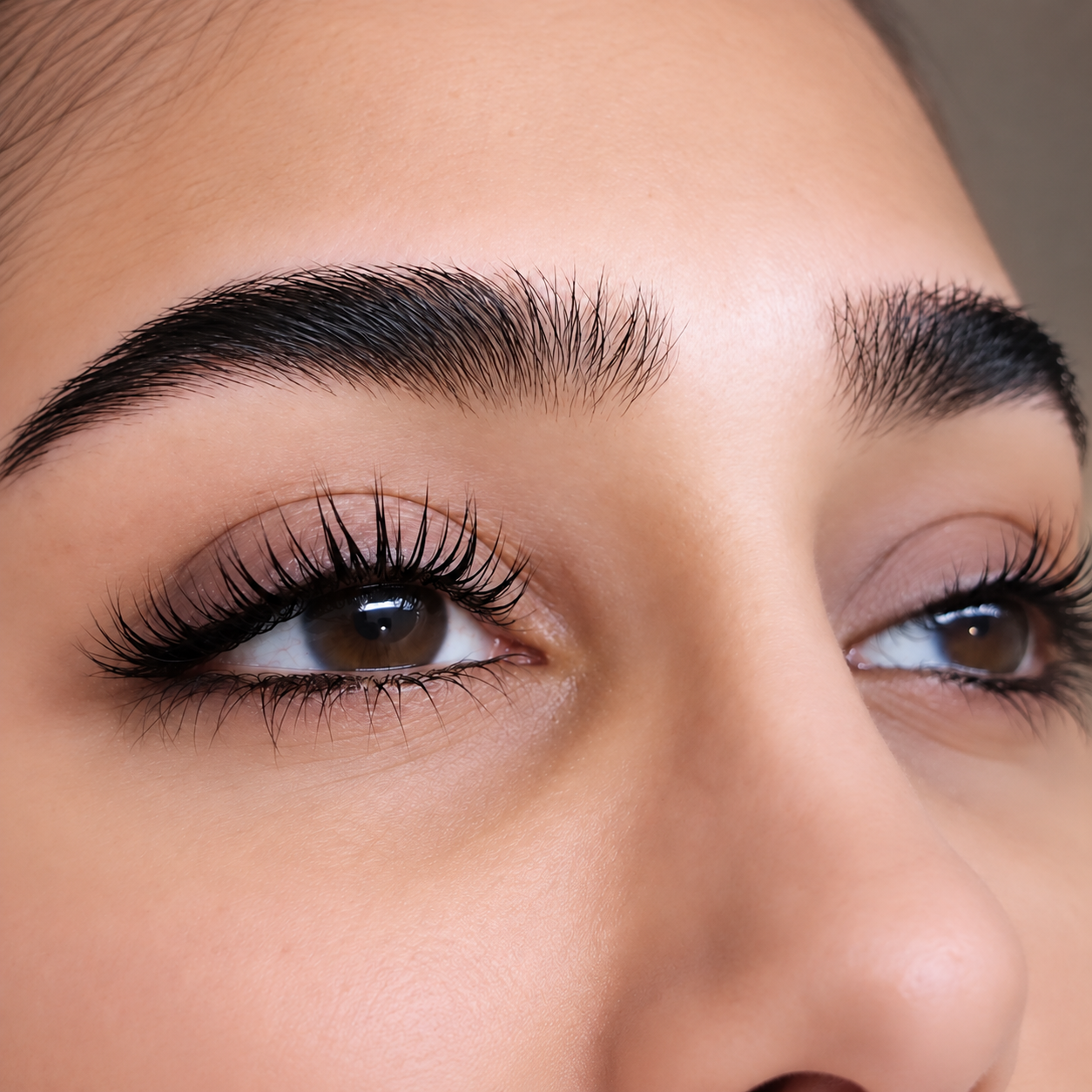 Close-up of a woman's eyes, showcasing well-groomed eyebrows, long eyelashes with mascara, and brown eyes.