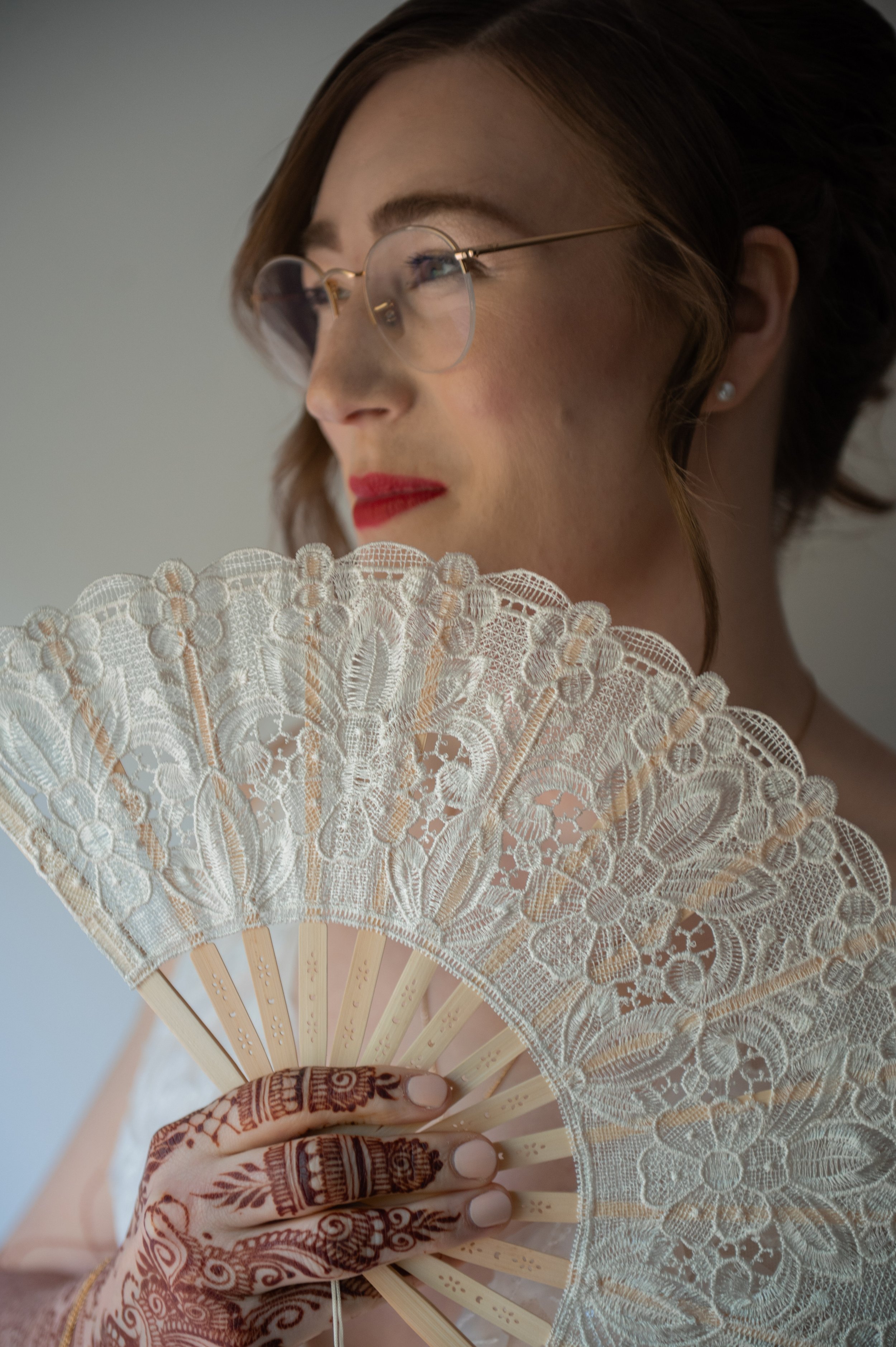 A woman with glasses holding an intricate lace hand fan.