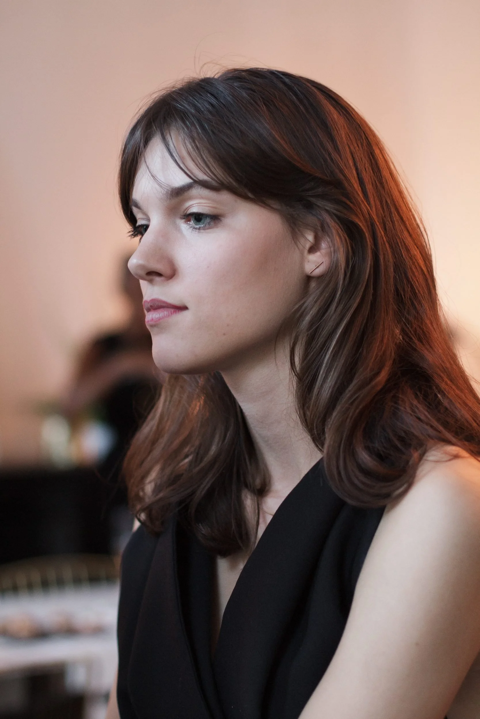 Profile portrait of a woman with reddish-brown hair wearing a black sleeveless top against a blurred interior background.