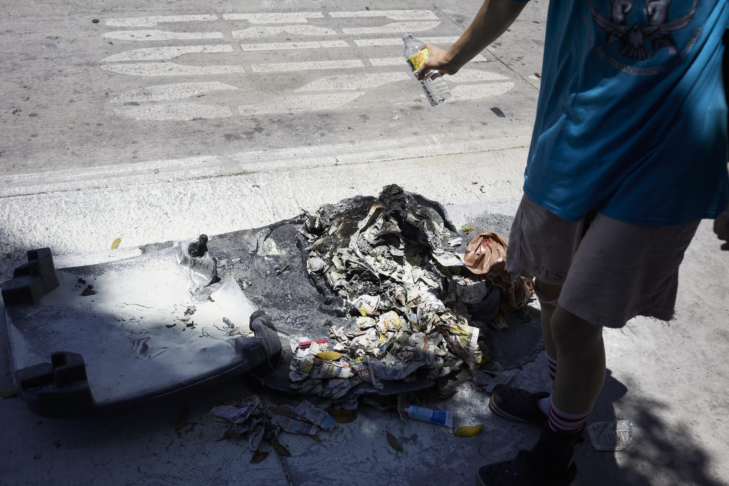 People examine burned debris and waste on a concrete surface.