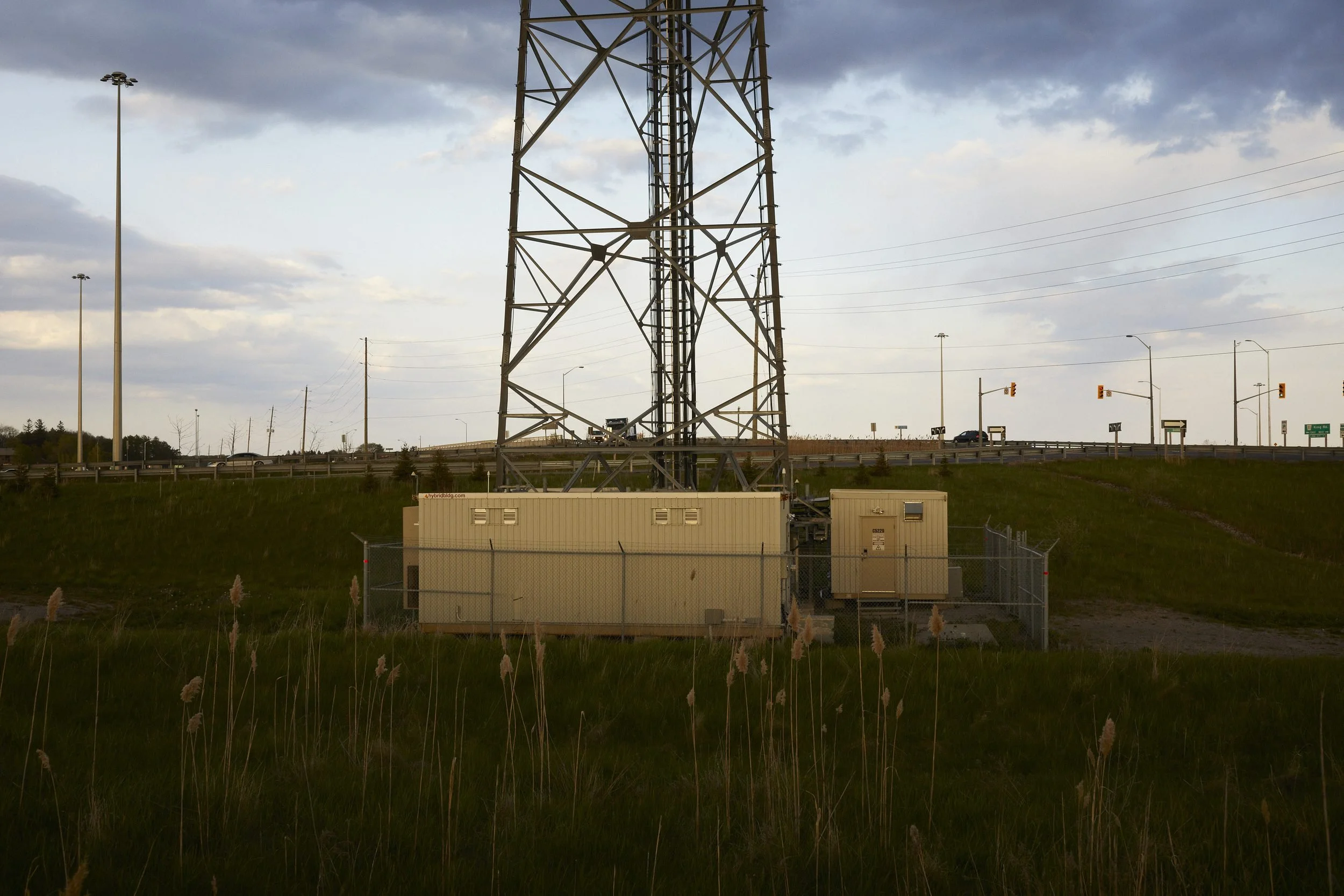 Industrial electrical substation with transformer equipment and transmission tower in rural grassland.
