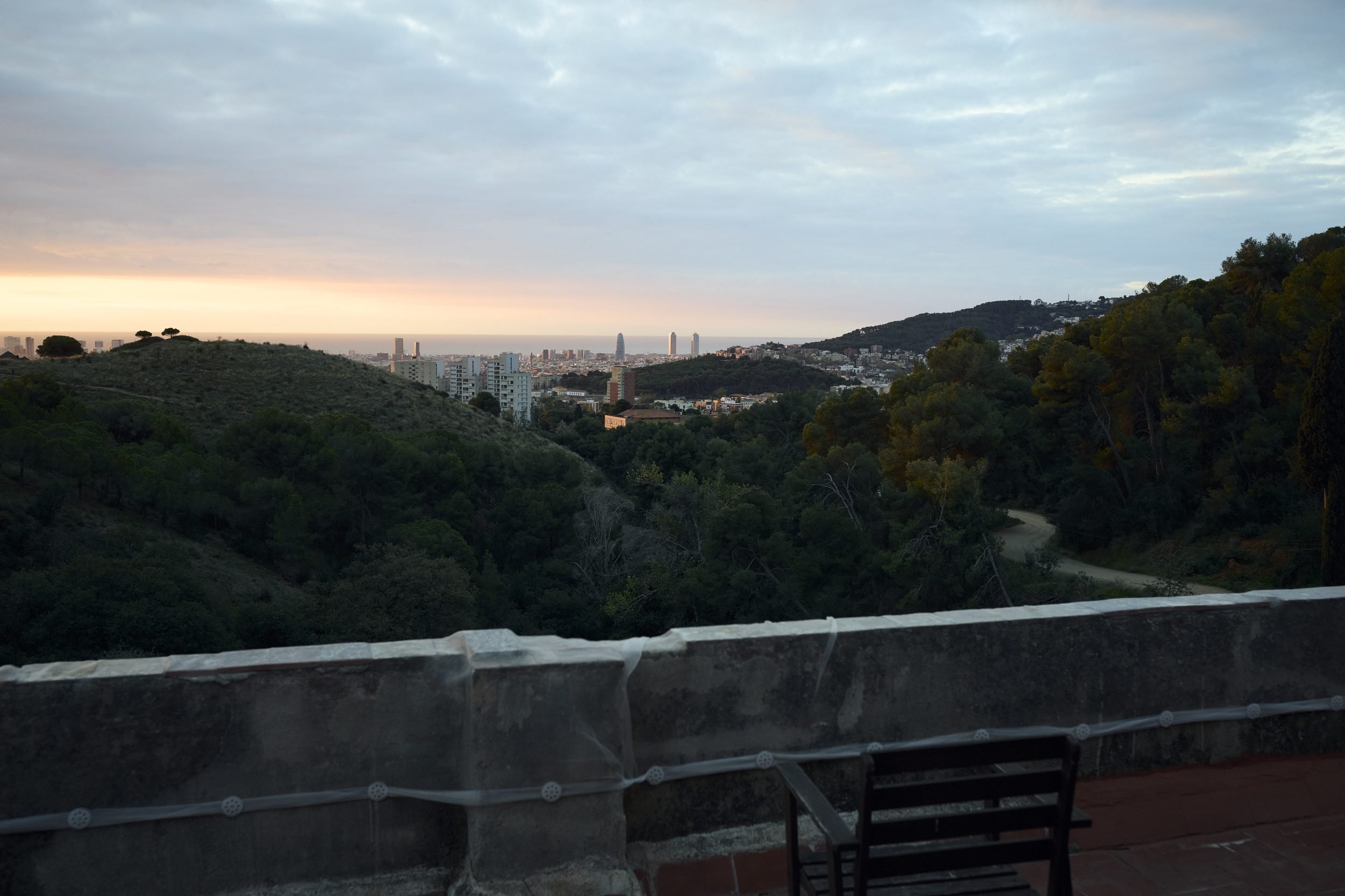 View from an overlook across forested hills toward a distant city skyline at dusk.