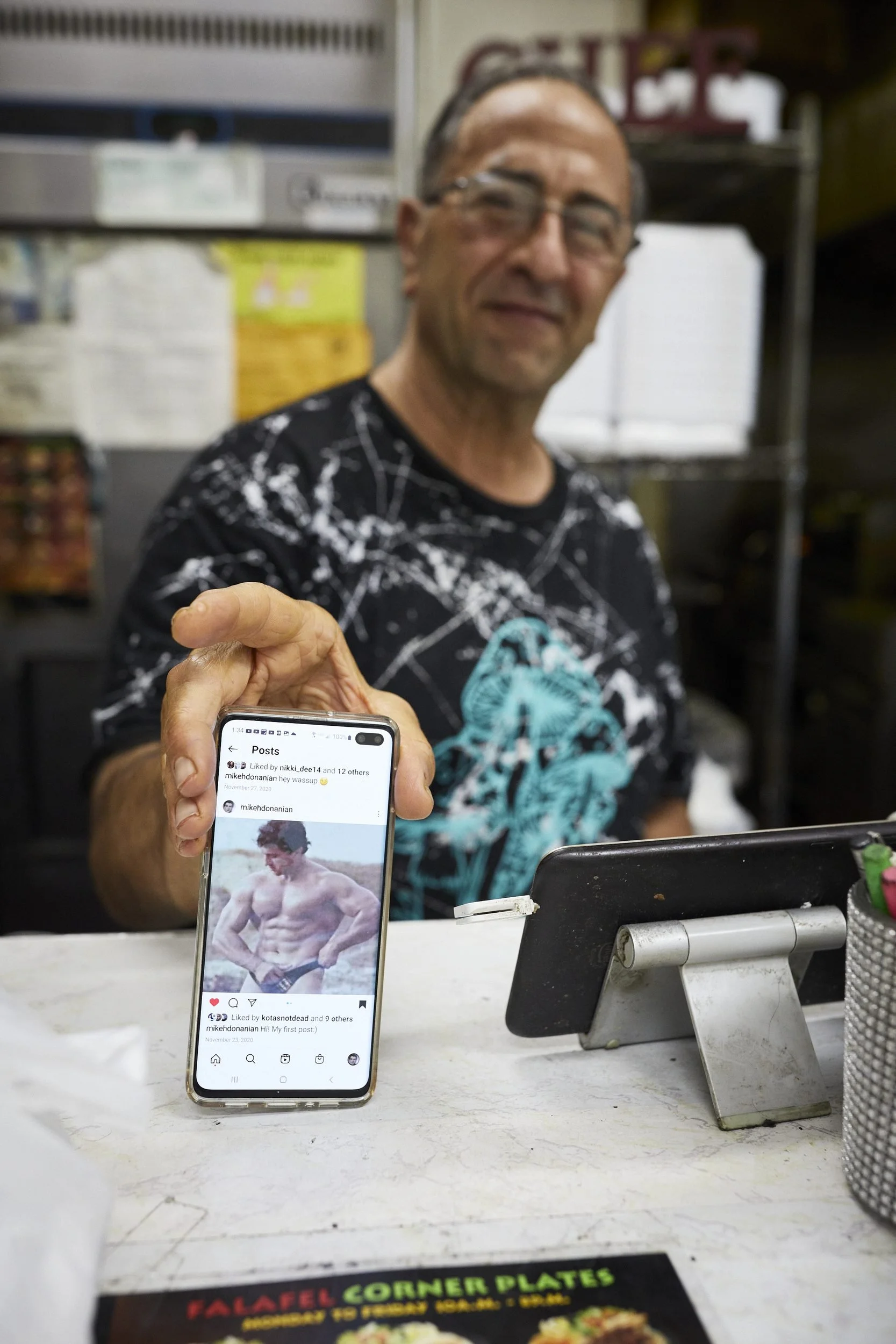 Man holding smartphone displaying a social media post in an office or workspace setting.