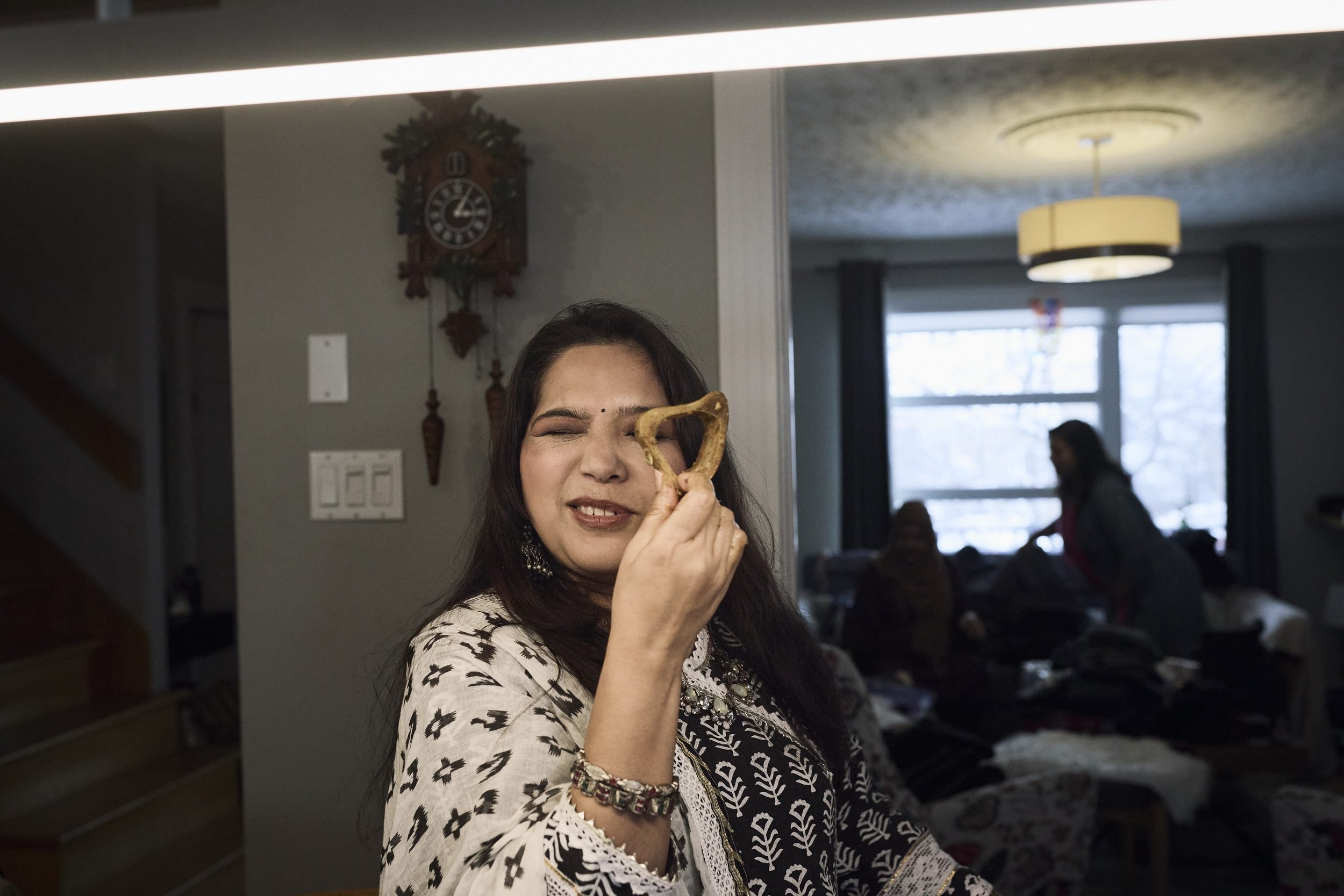 A woman holds a gold-colored object near her face while smiling in an indoor space with a cuckoo clock on the wall.