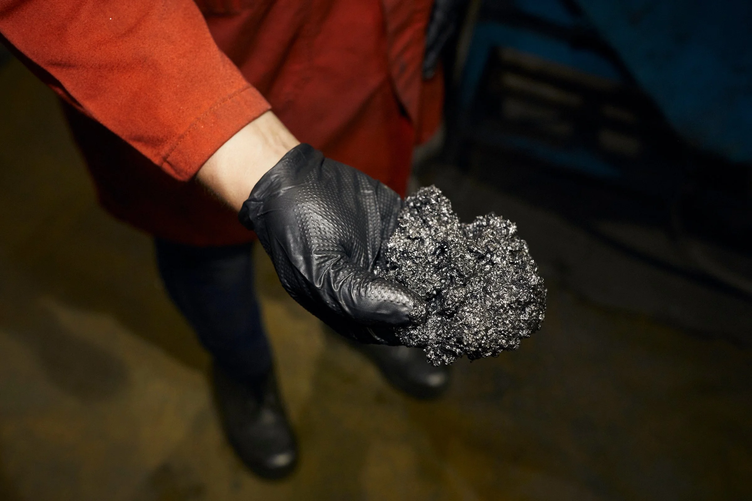 A gloved hand holds a lump of metallic grey graphite at Nouveau Monde Graphite, Saint-Michel-des-Saints, Quebec.