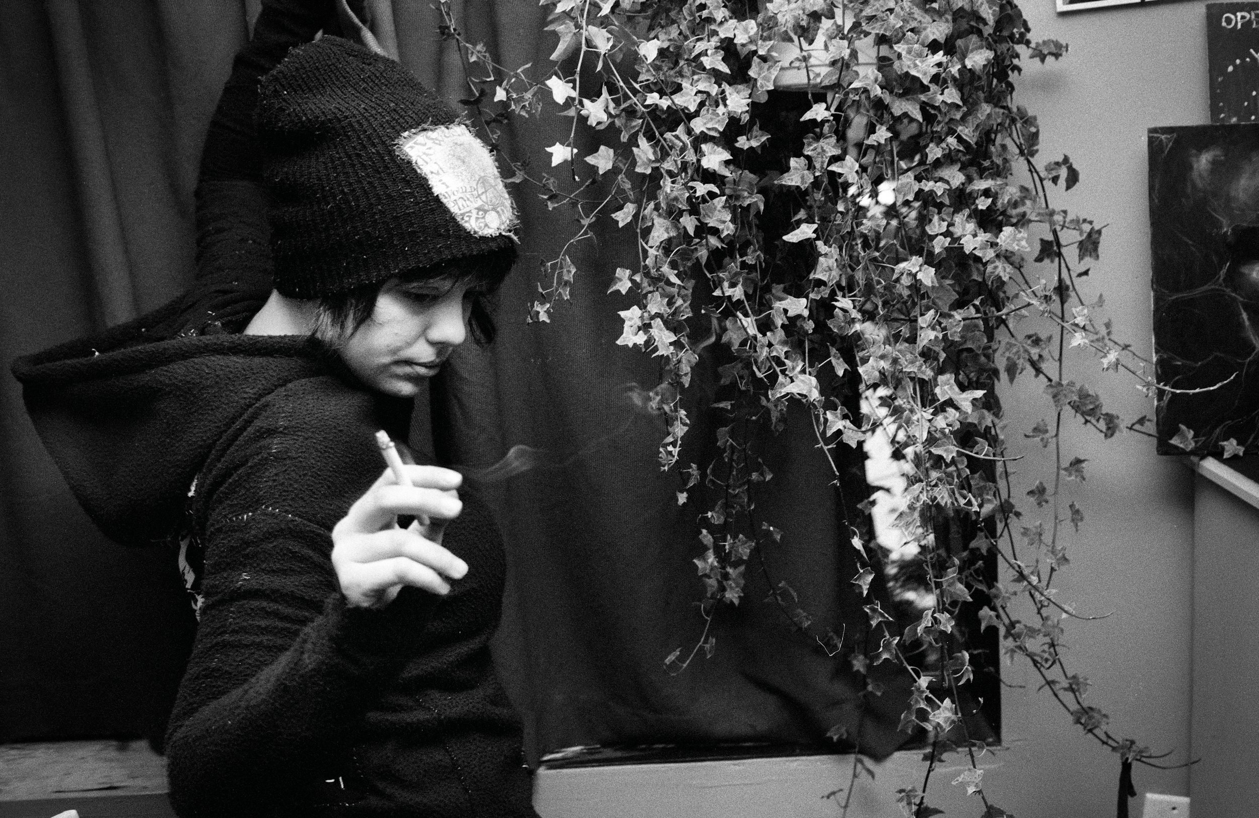 Child in black winter clothing reaches toward dried vines and flowers hanging on a wall.