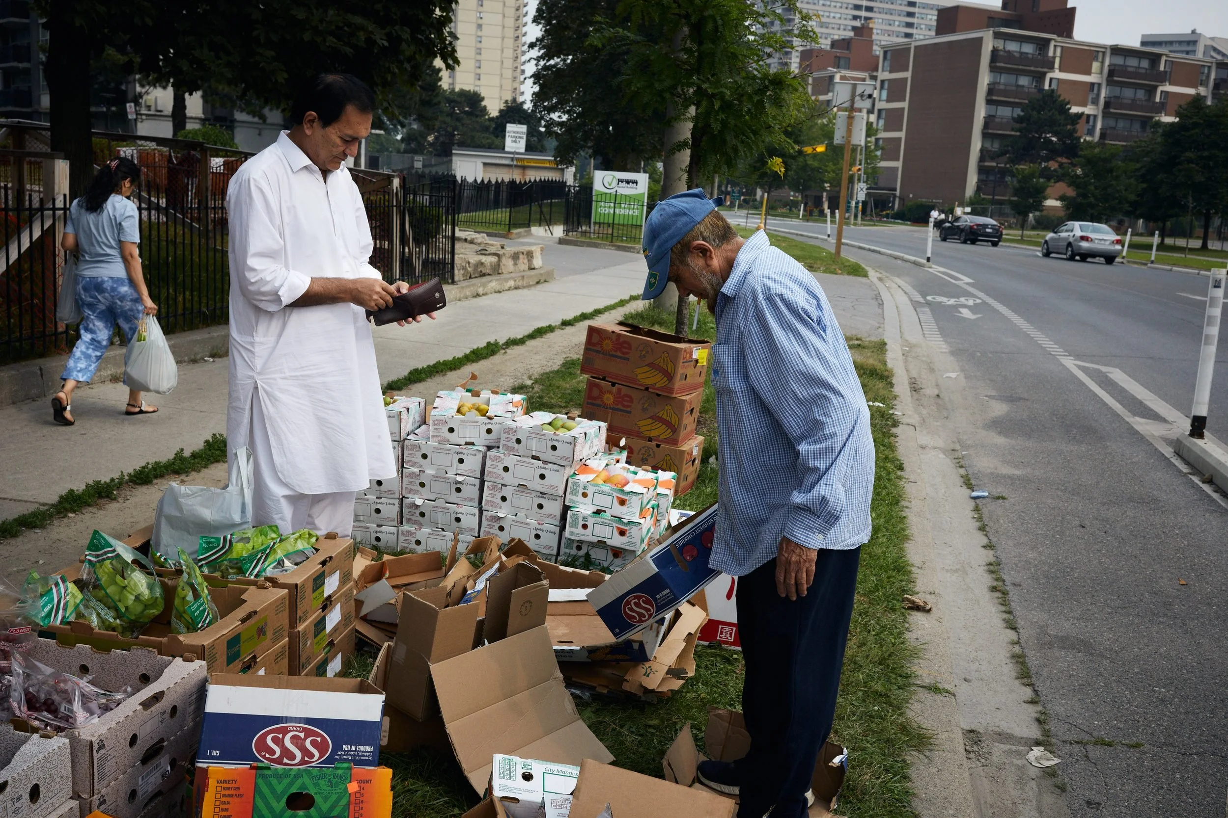 A man buys fruit from a fruit-seller in front of 75 Thorncliffe Park Drive.