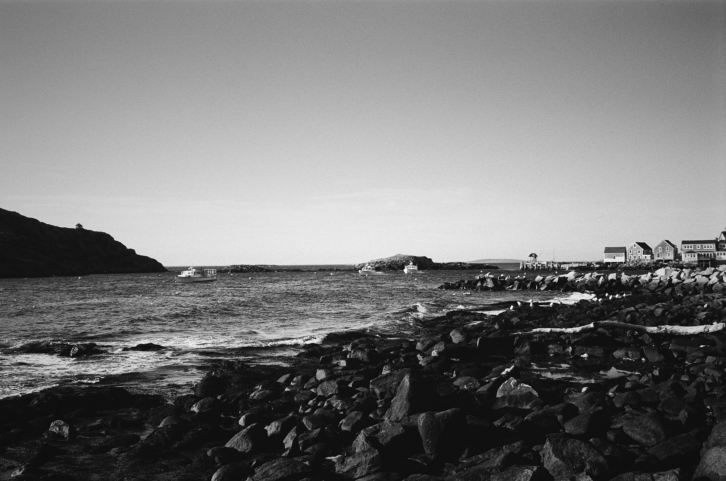 Rocky coastline with houses and buildings visible across the water under overcast sky.