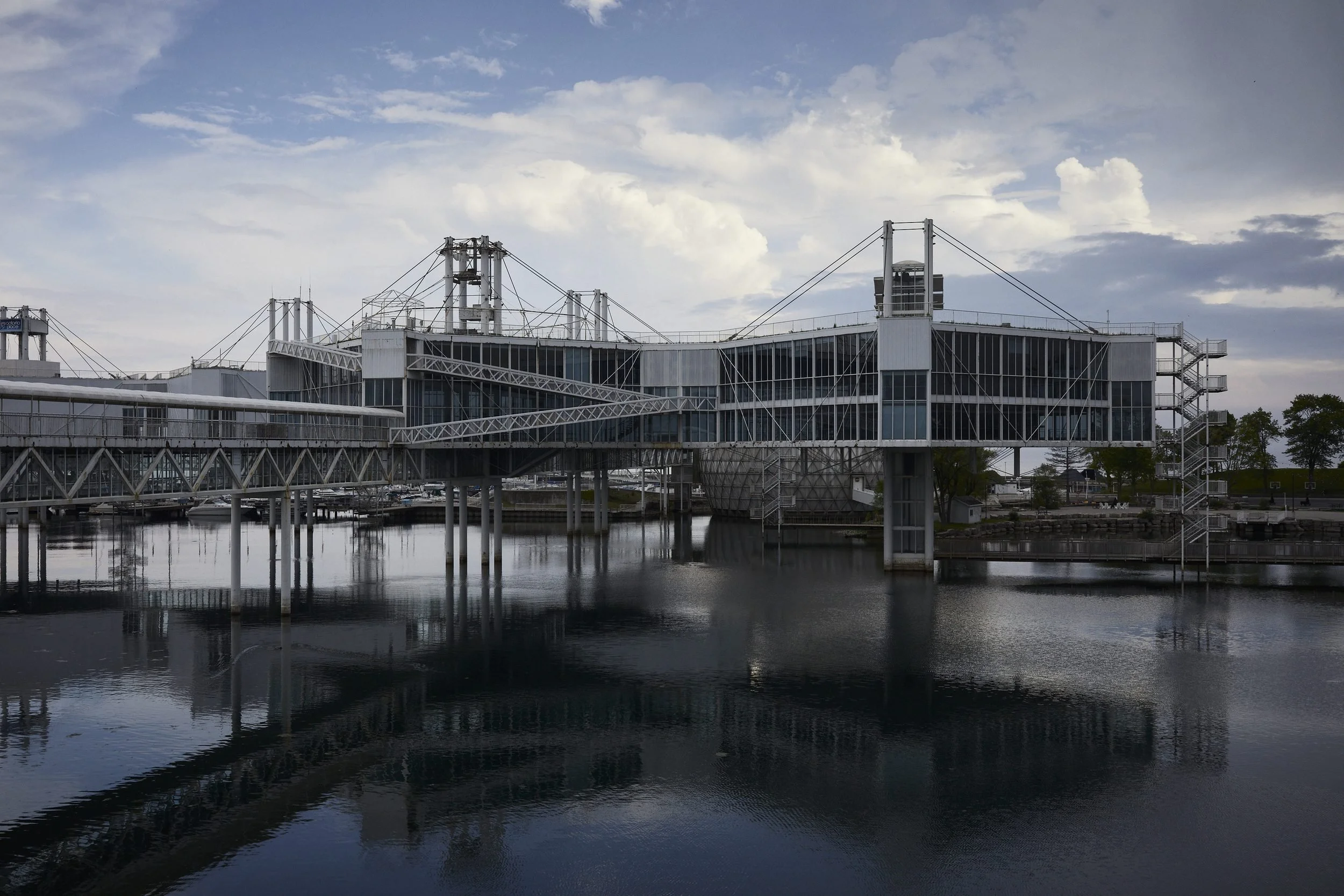 Industrial waterfront complex with suspension bridges and steel structures reflected in still water.